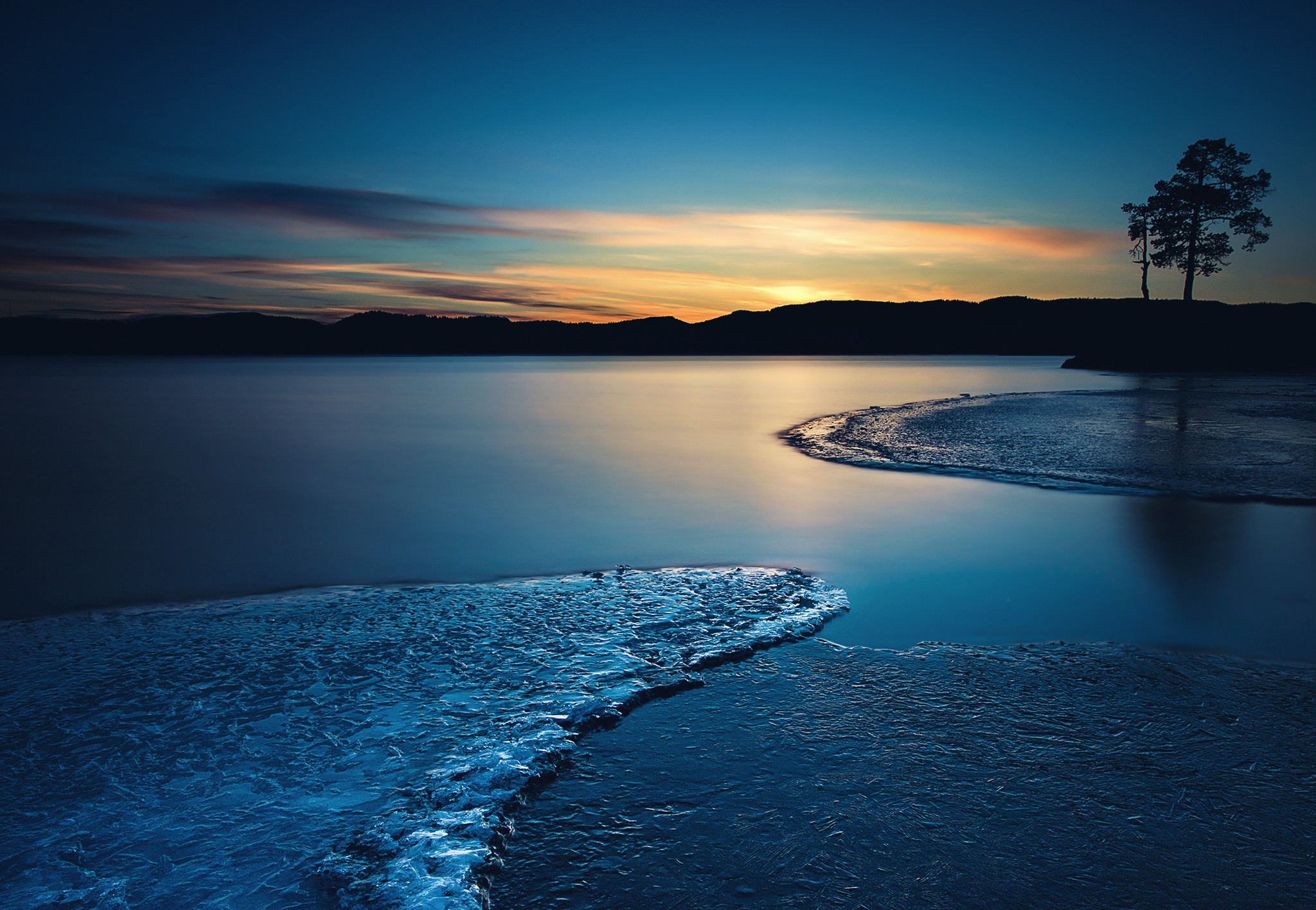 Frozen lake at sunset with silhouetted trees HD Wallpaper