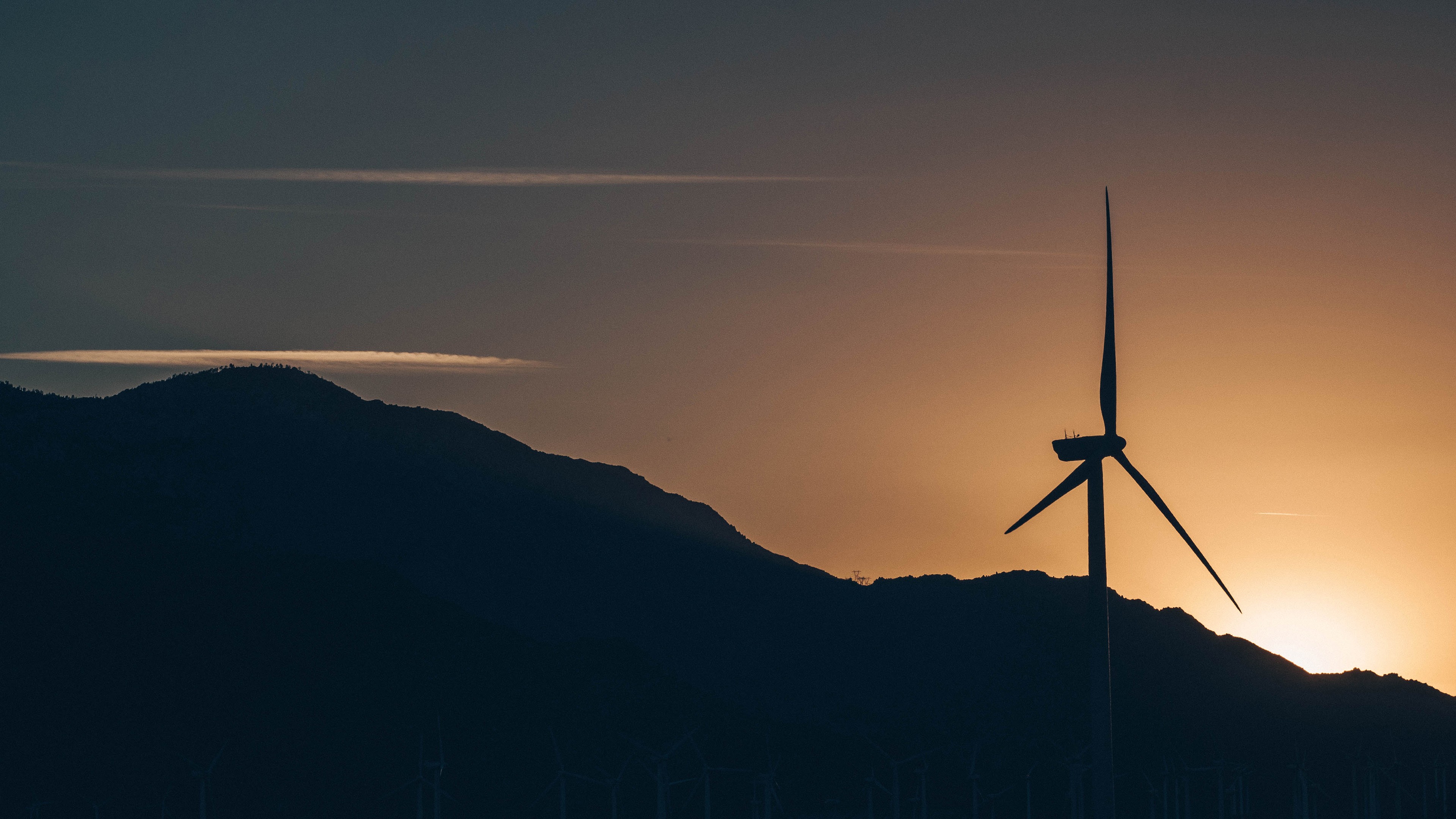 Silhouette of a windmill against a sunset over mountains HD Wallpaper