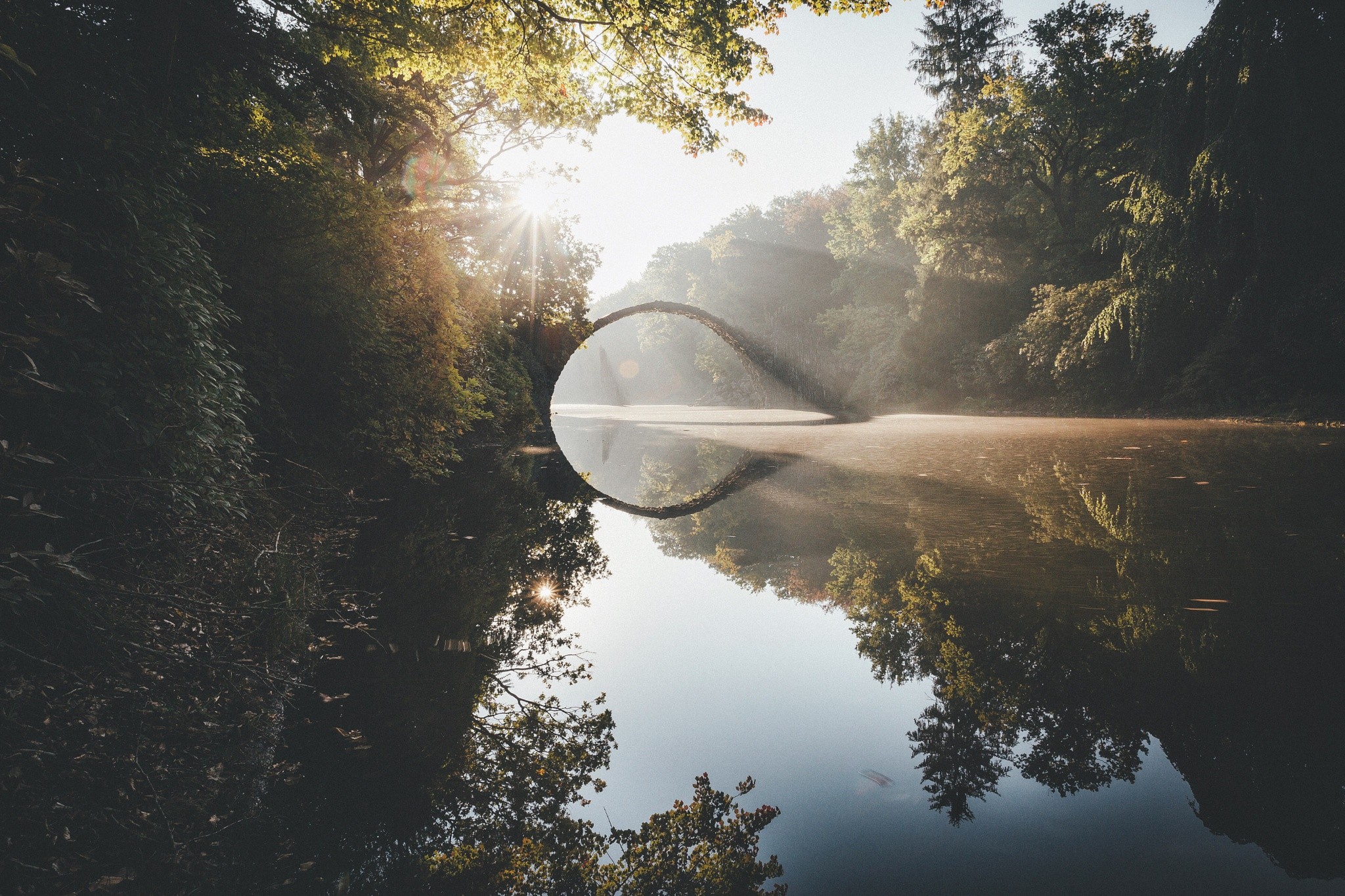 Arch bridge reflecting in a misty pond at sunrise HD Wallpaper