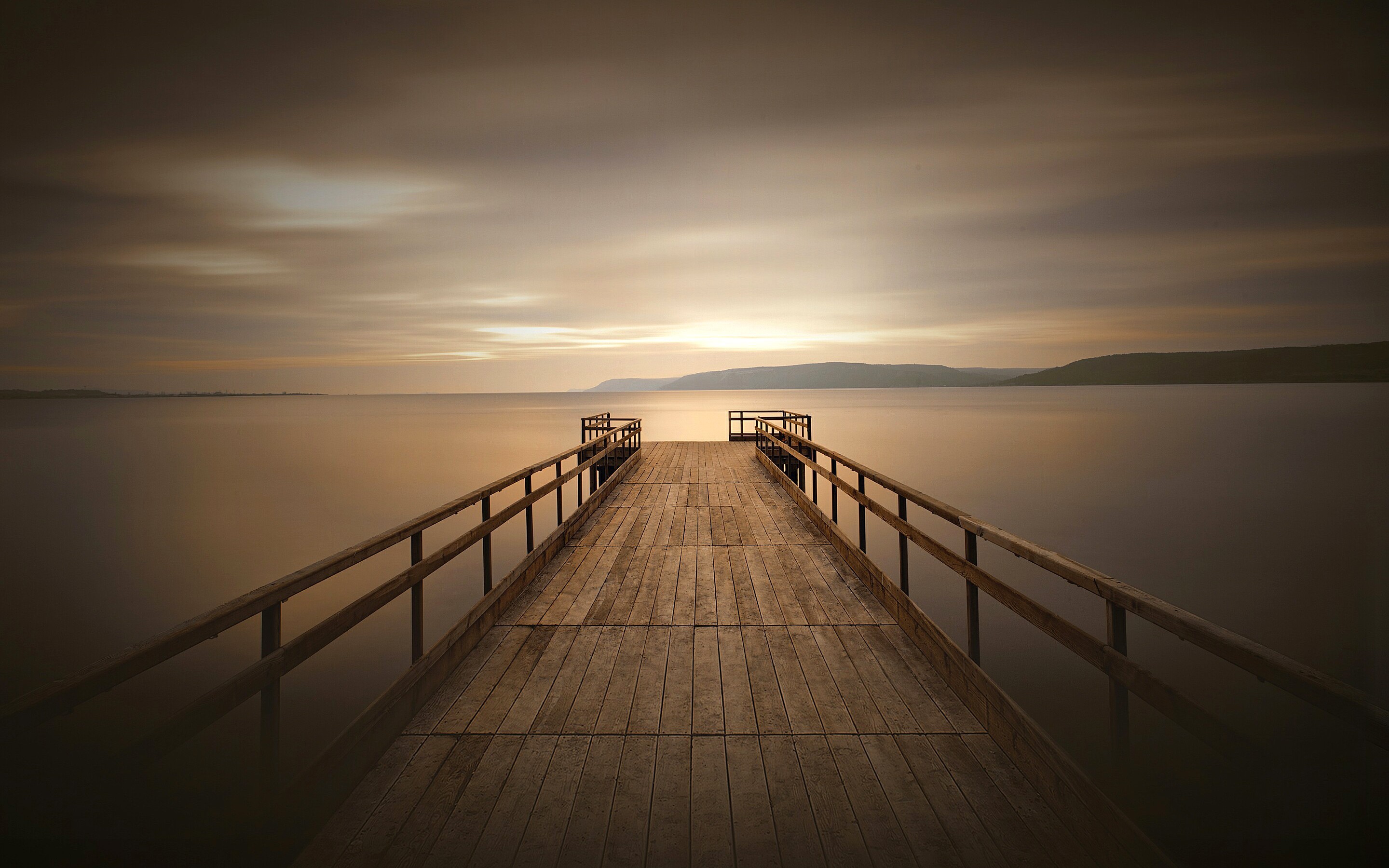 Wooden pier extending into a calm body of water at sunset HD Wallpaper