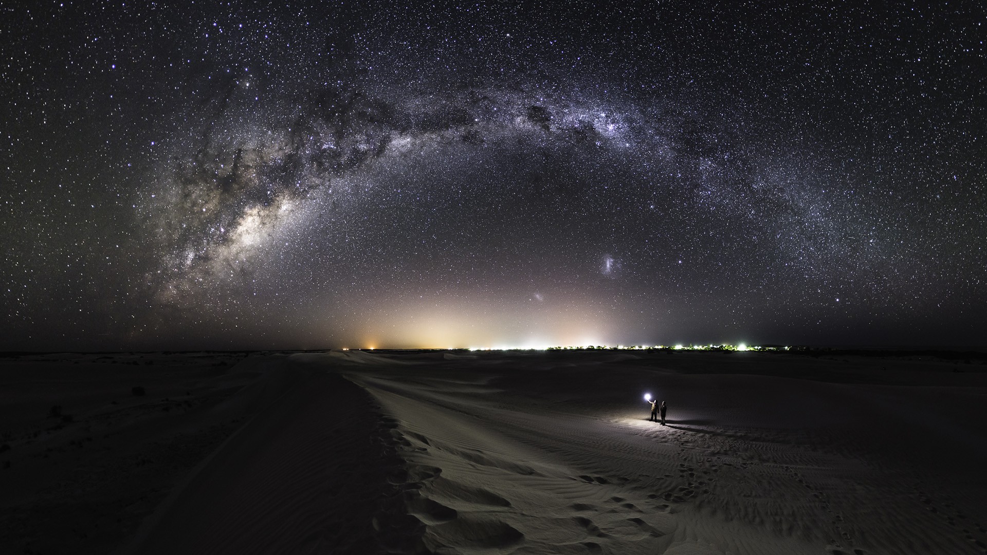 Milky Way galaxy over desert landscape with two people HD Wallpaper