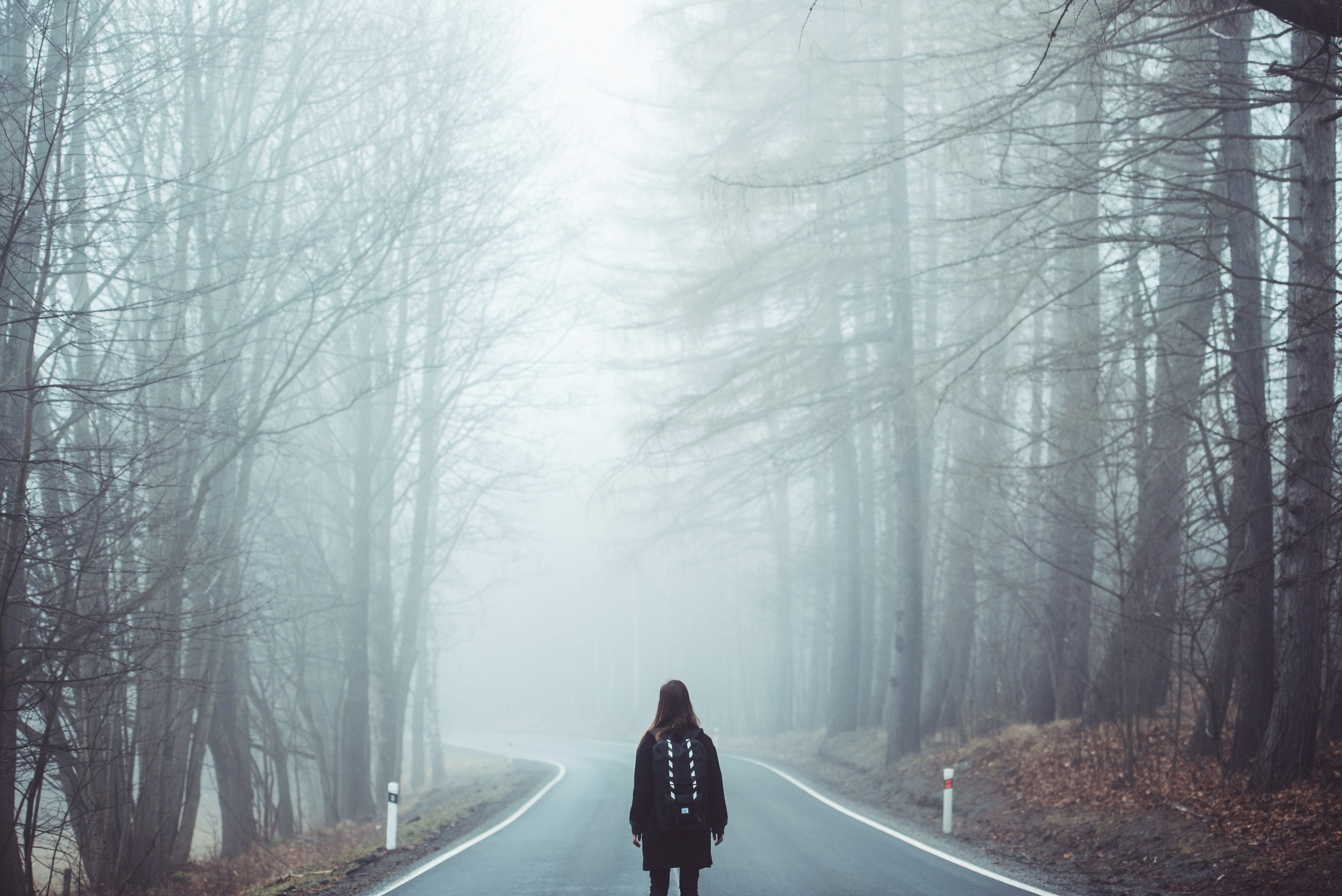 Woman with backpack on foggy road through trees HD Wallpaper