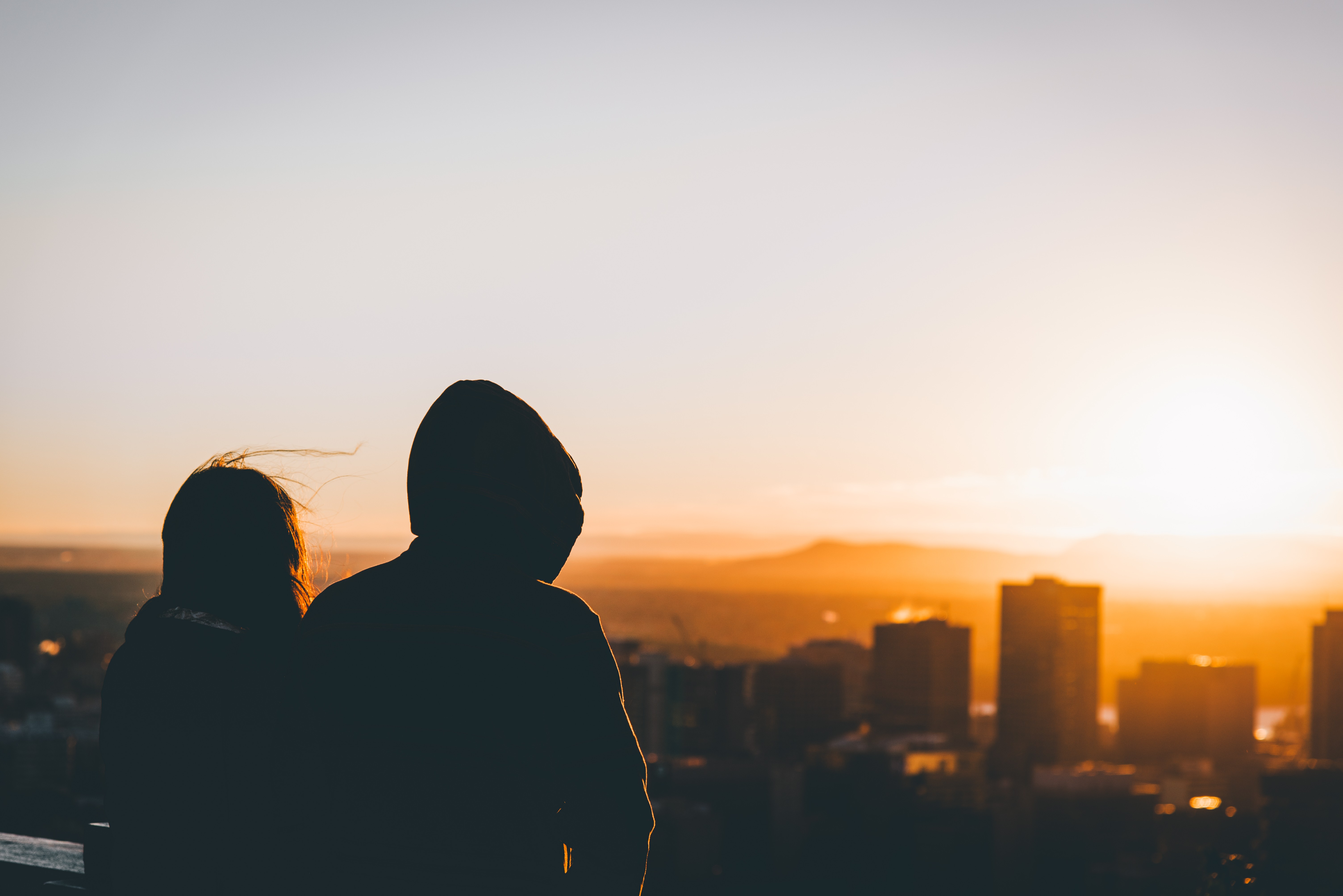 Two people silhouetted against a sunset over a city HD Wallpaper