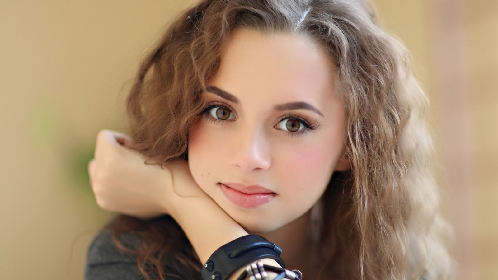 Young woman with curly hair resting her chin on her hand HD Wallpaper