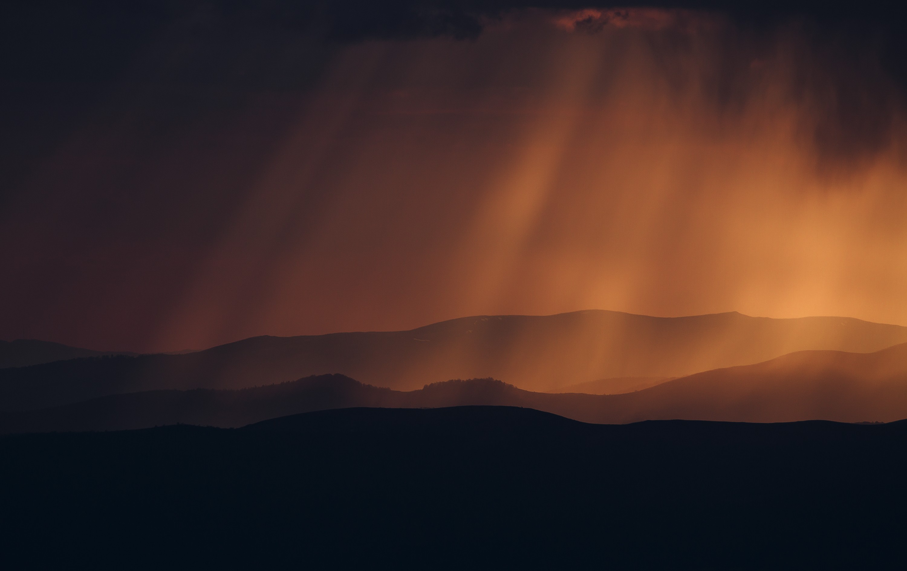 Sun rays over silhouetted hills at sunset HD Wallpaper