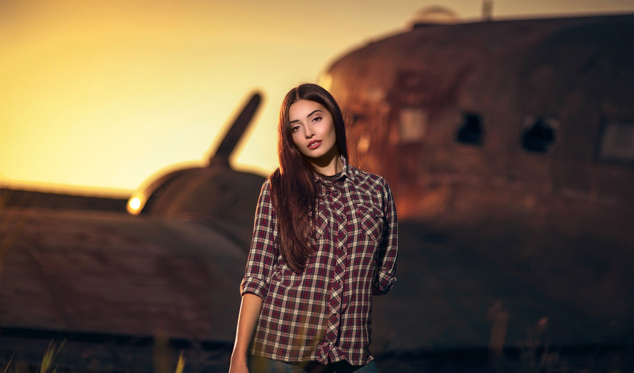 Woman in plaid shirt in front of airplane at sunset HD Wallpaper