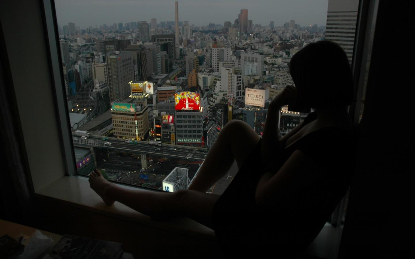 Woman sitting by window overlooking Tokyo cityscape at dusk HD Wallpaper
