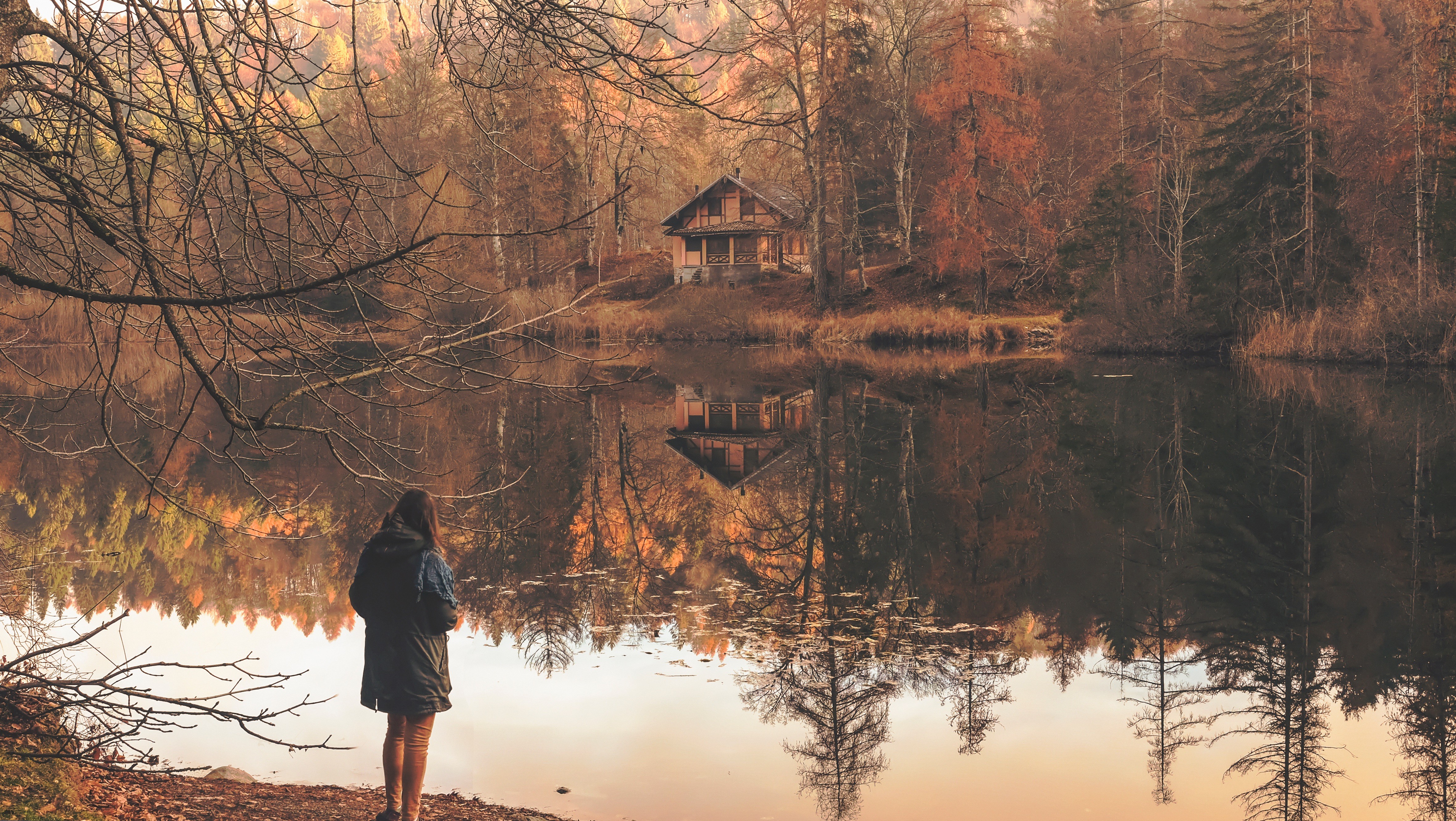 Person by lake with house in autumn forest HD Wallpaper