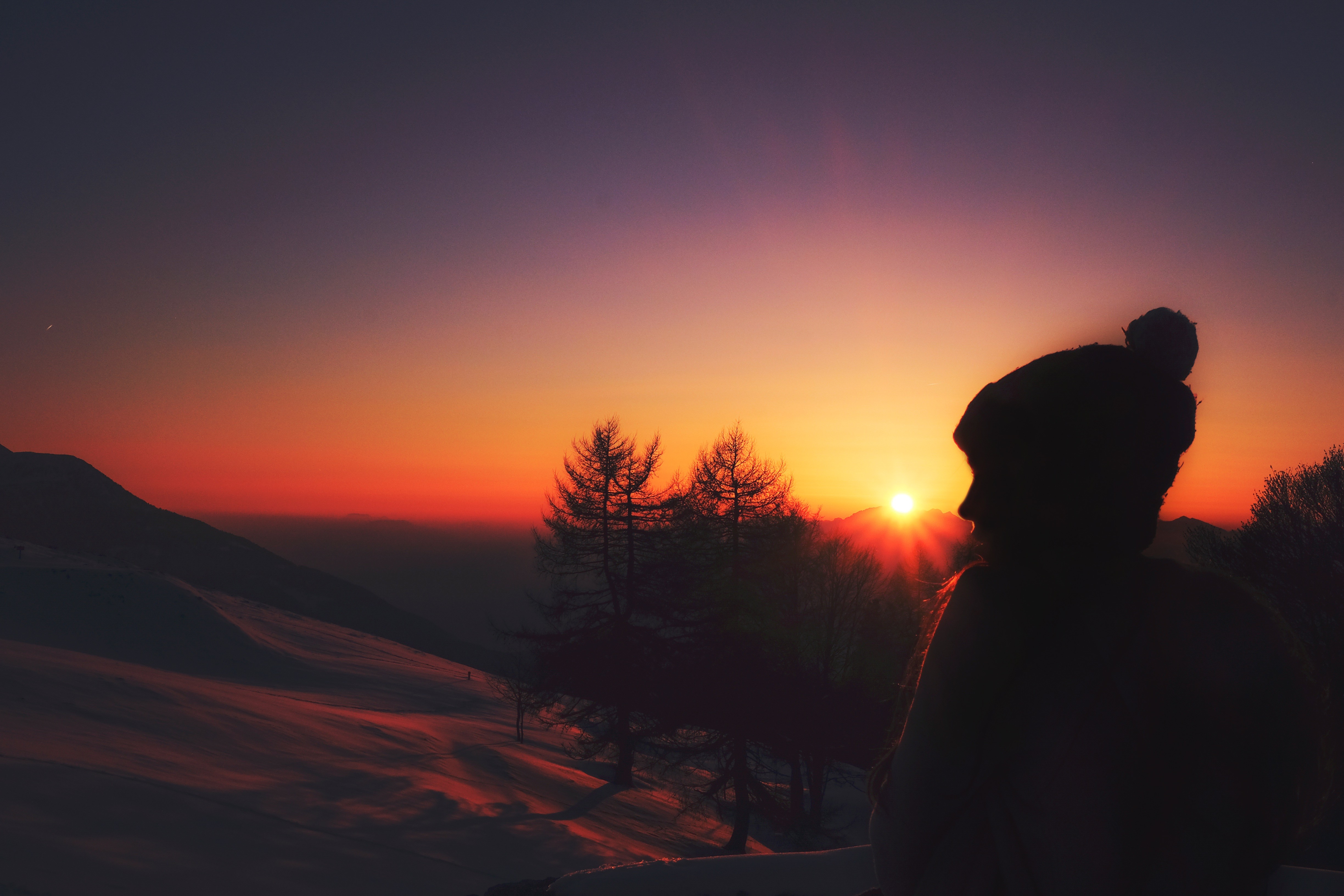 Silhouette of a person watching a sunset over a snowy landscape HD Wallpaper