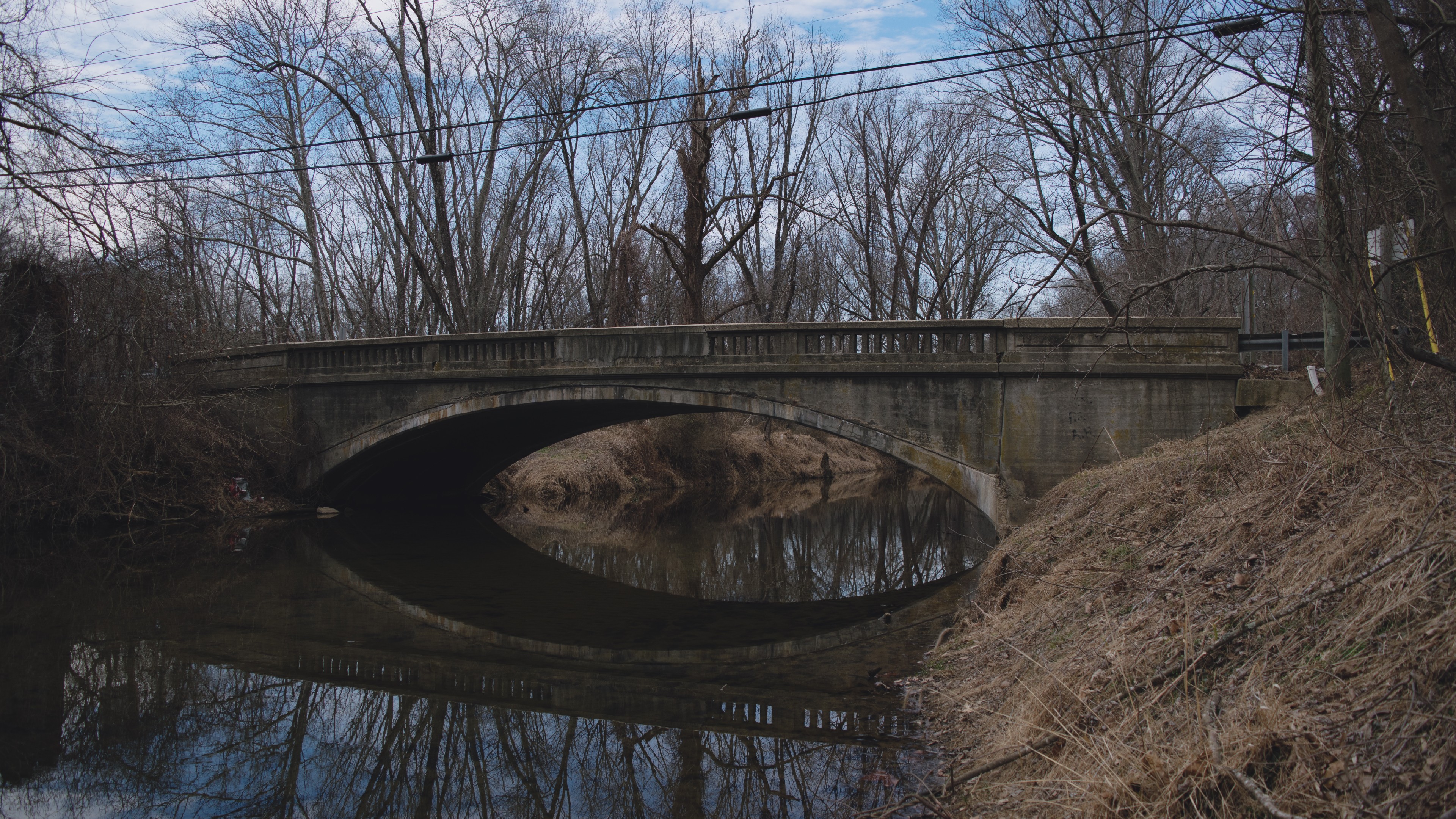 Concrete arch bridge over a calm river with bare trees HD Wallpaper