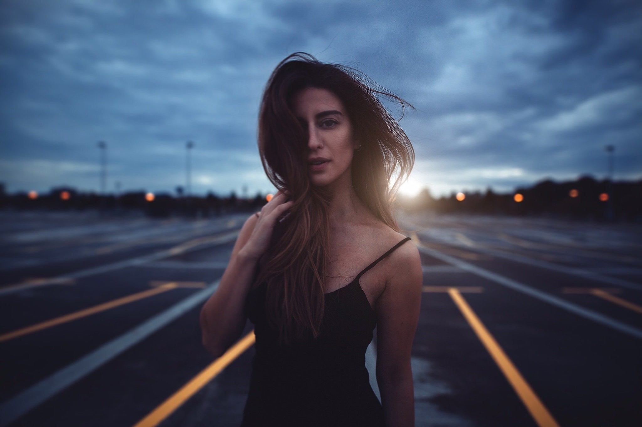 Woman in a black dress in a parking lot at dusk HD Wallpaper