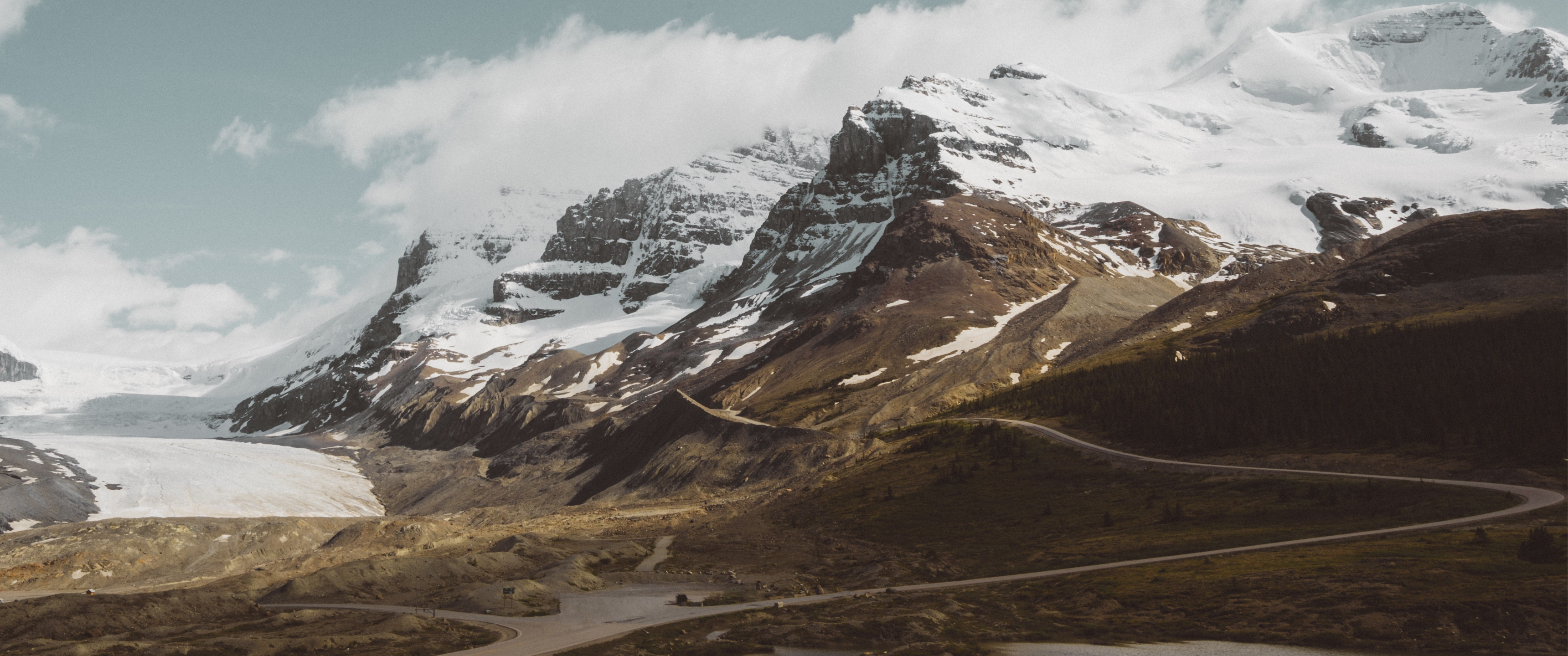 Snow-capped mountains and a winding road HD Wallpaper