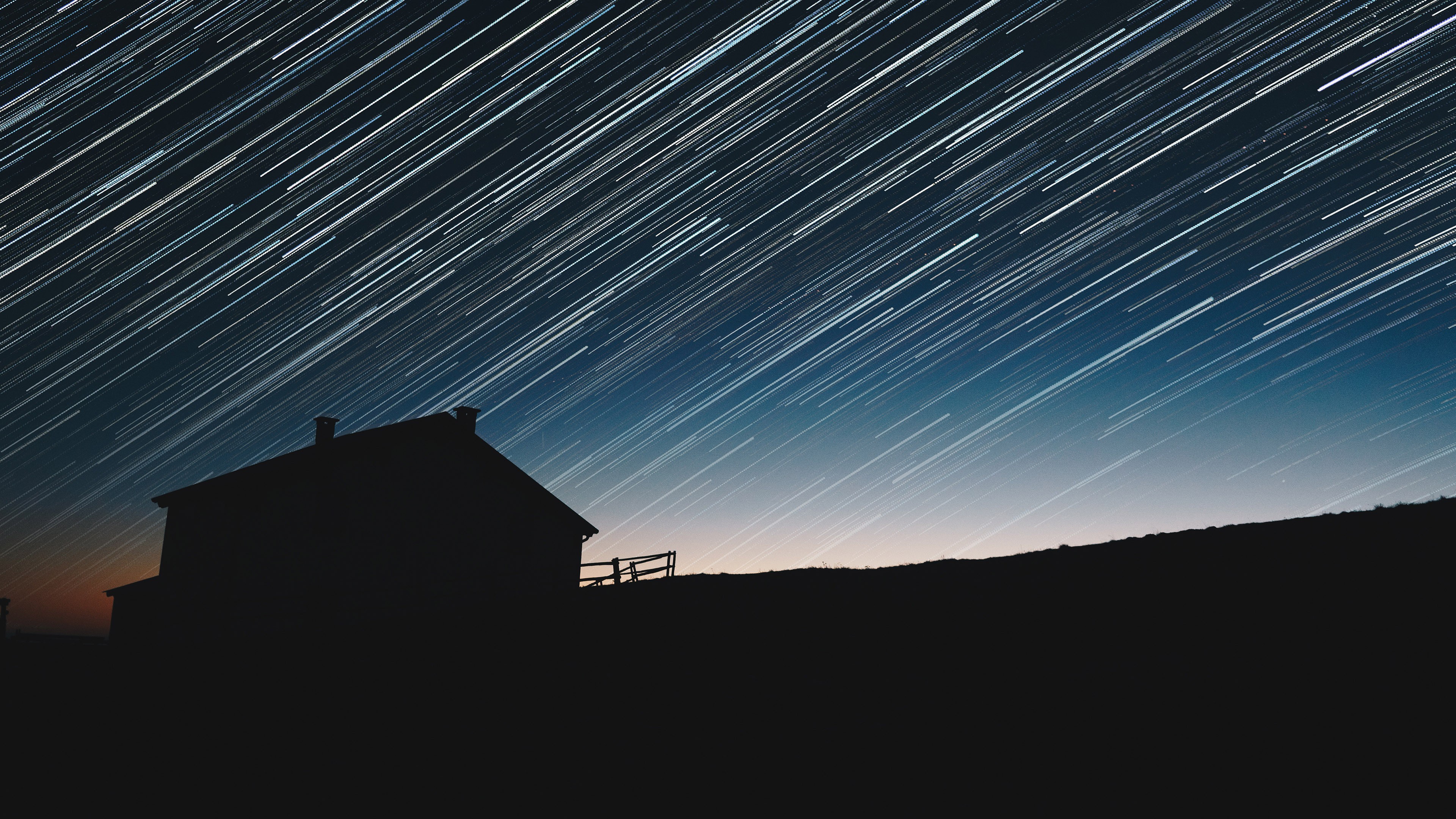 Star trails over a silhouetted house at night HD Wallpaper