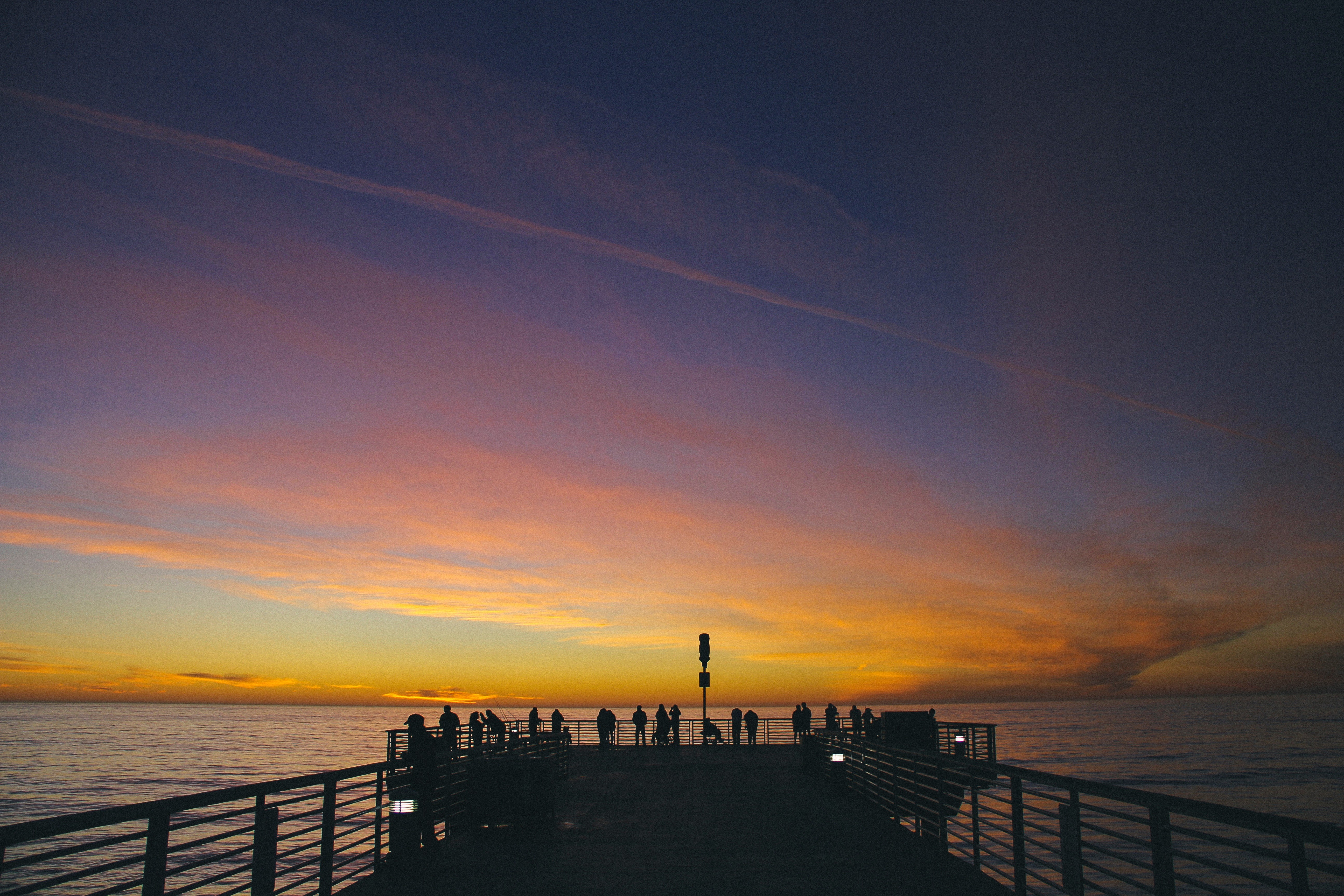 People on a pier watching a sunset over the ocean HD Wallpaper