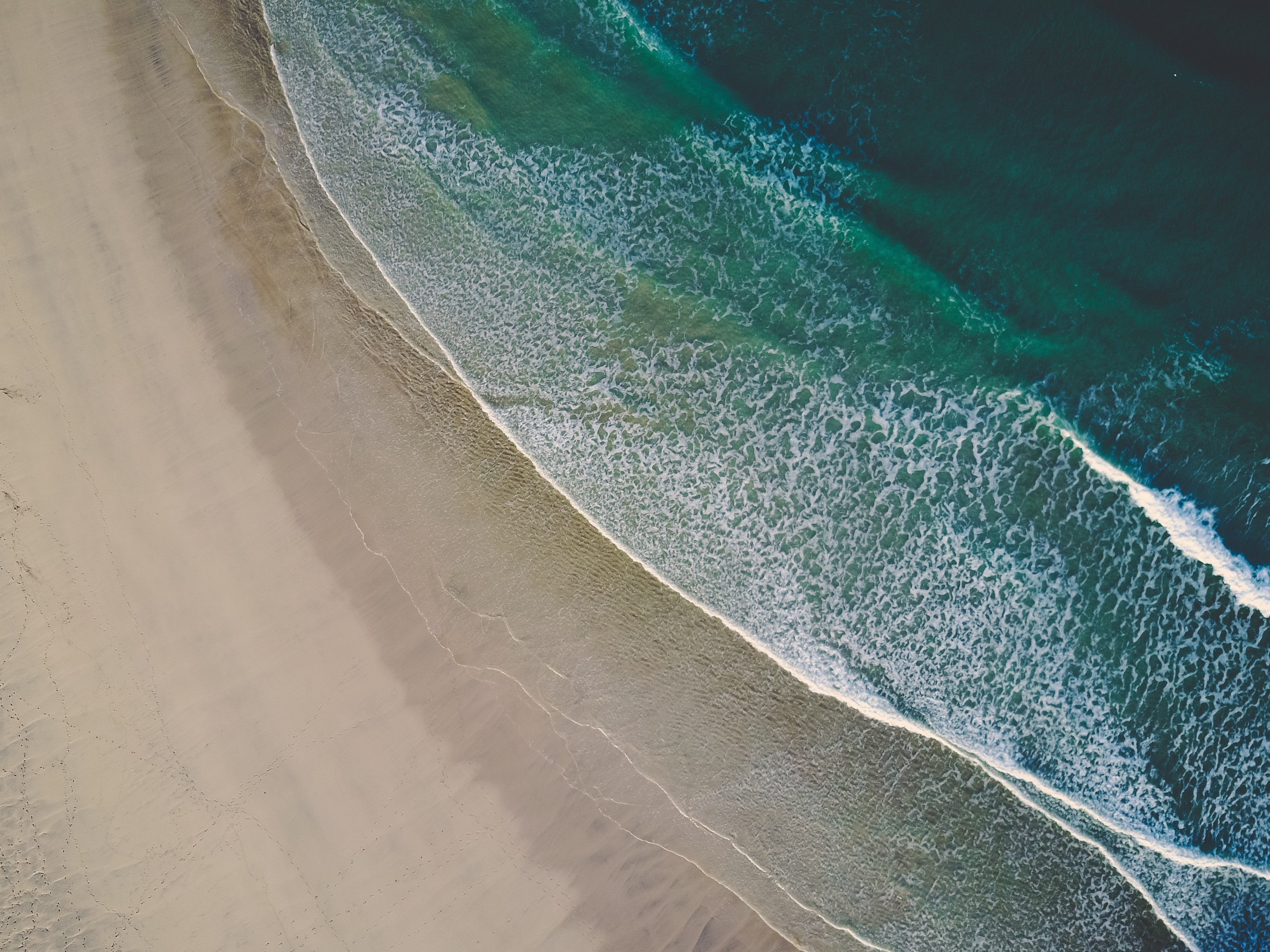 Aerial view of a sandy beach with ocean waves HD Wallpaper