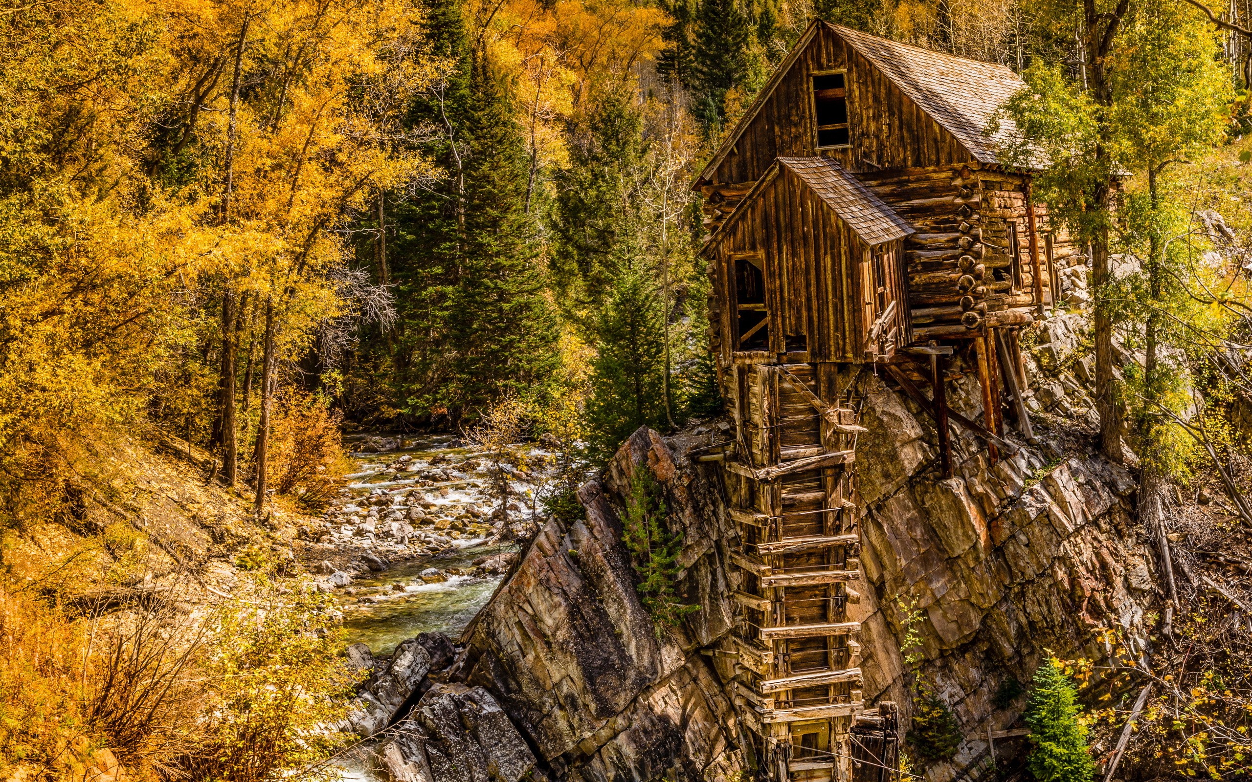 Old wooden mill on a cliffside with a river and autumn trees HD Wallpaper