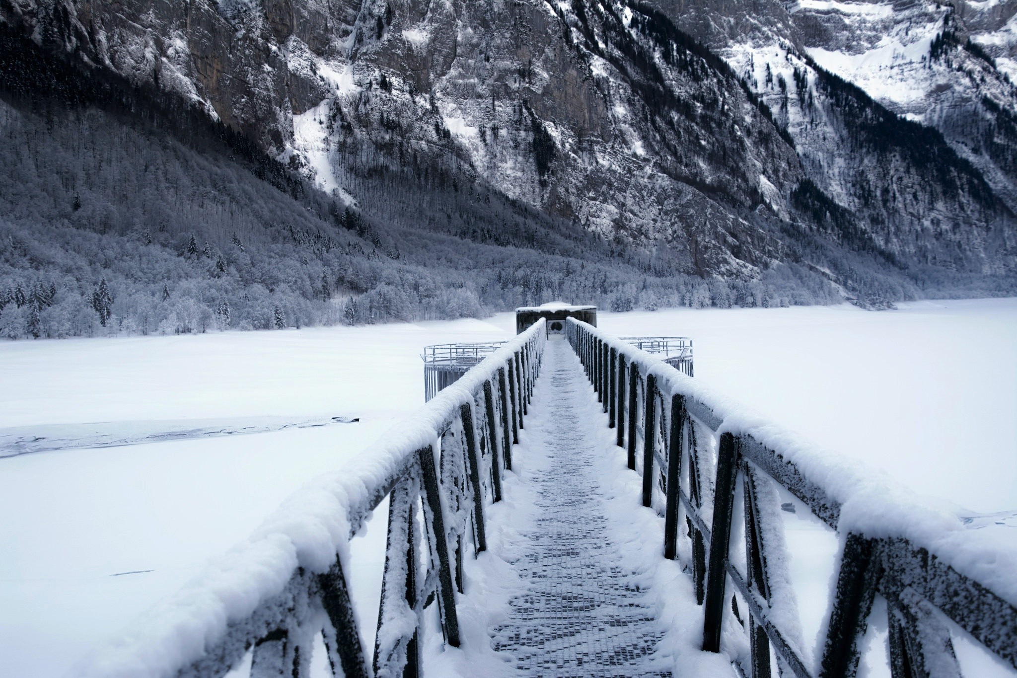 Snow-covered bridge over a frozen lake with mountains HD Wallpaper