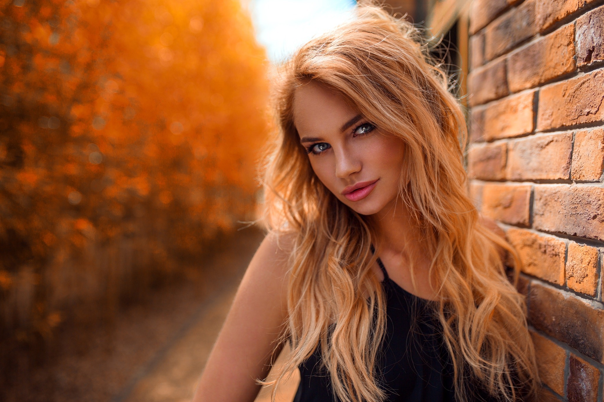 Woman with blonde hair leaning against a brick wall HD Wallpaper