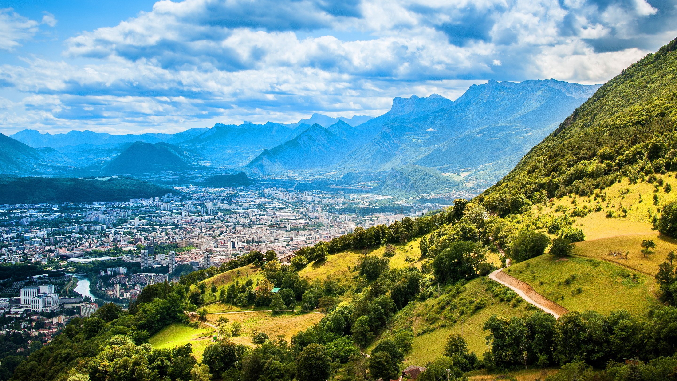 City nestled in a valley with mountains and green hills HD Wallpaper