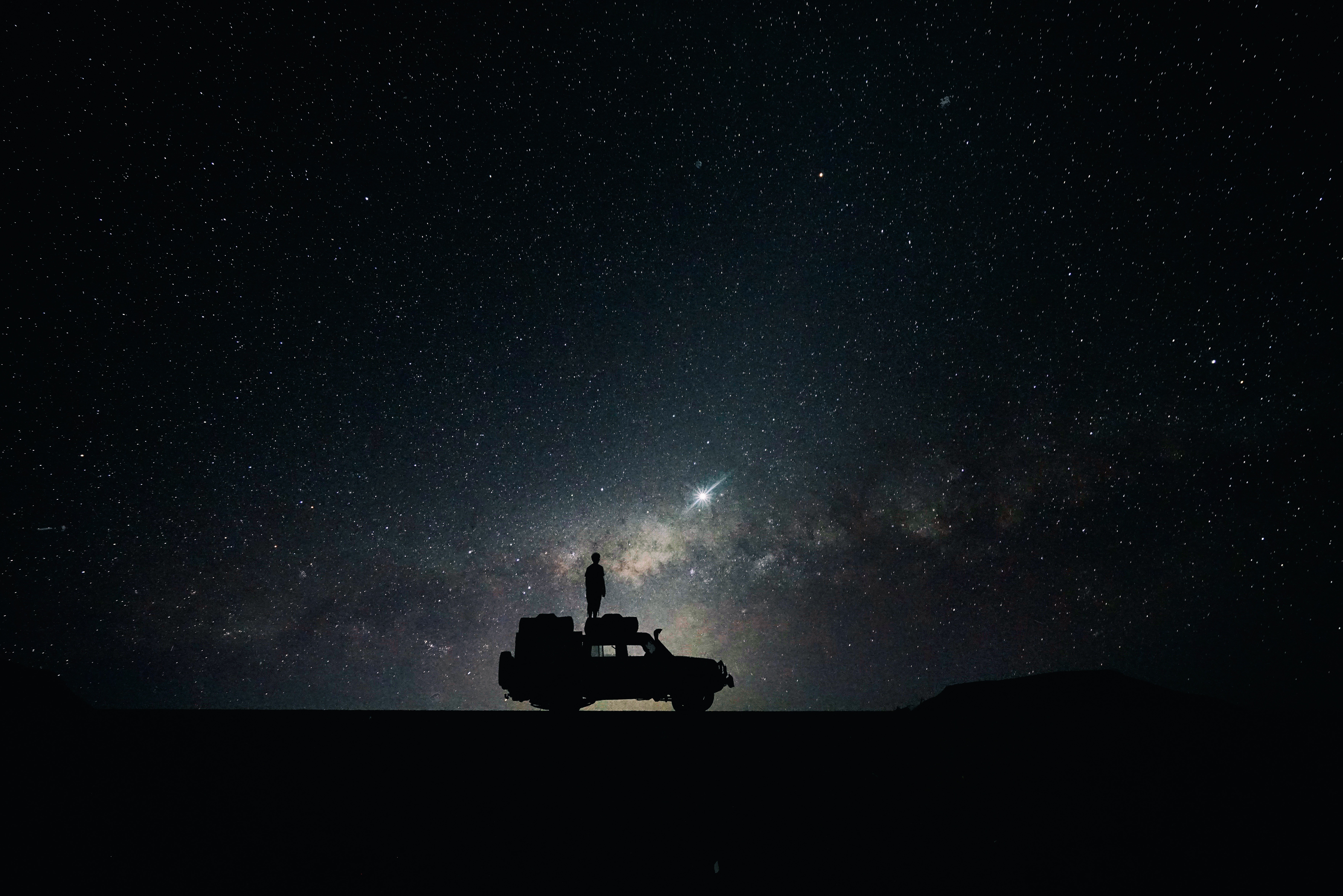 Person standing on a car under the starry night sky HD Wallpaper