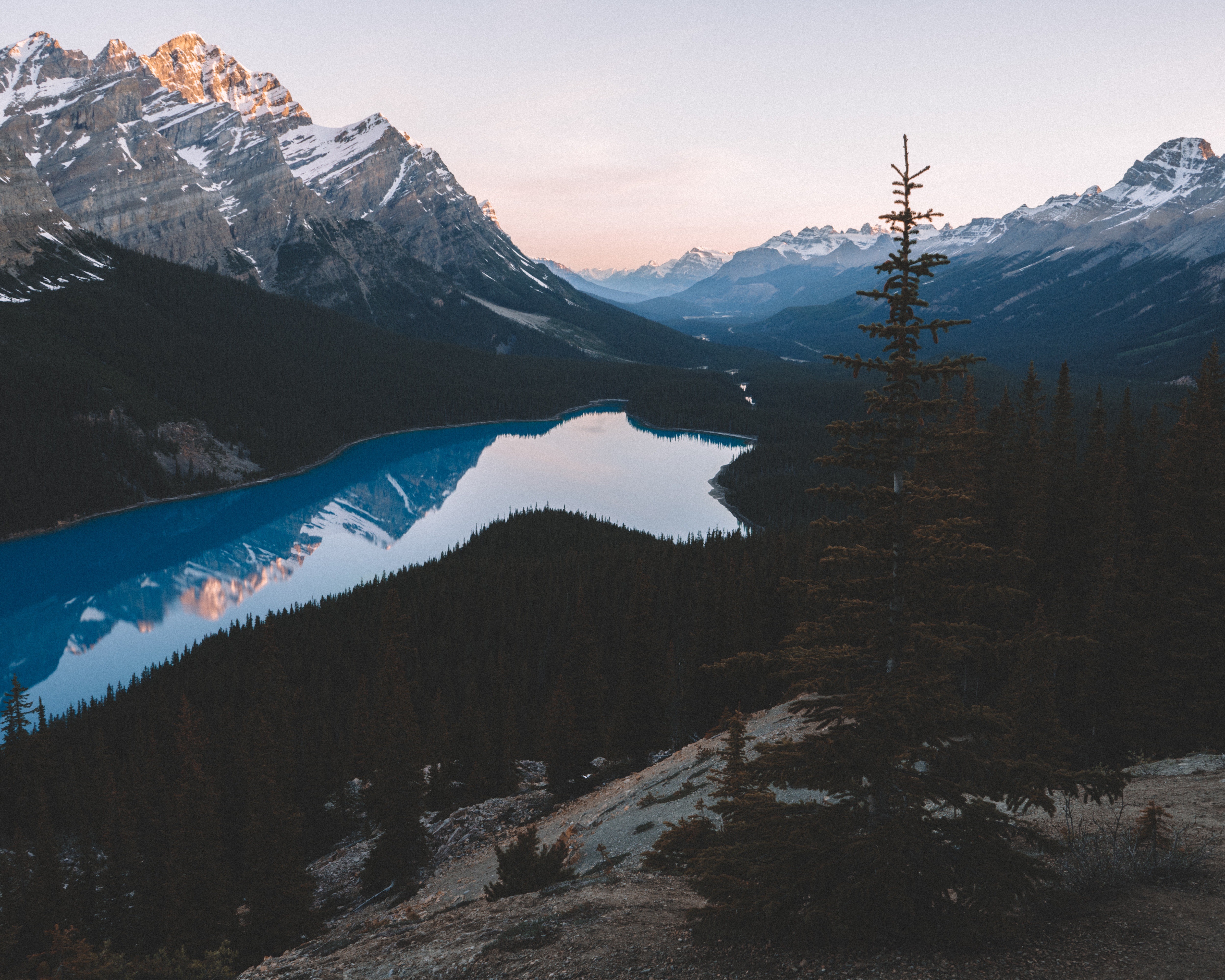 Snow-capped mountains reflecting in a blue lake surrounded by trees HD Wallpaper