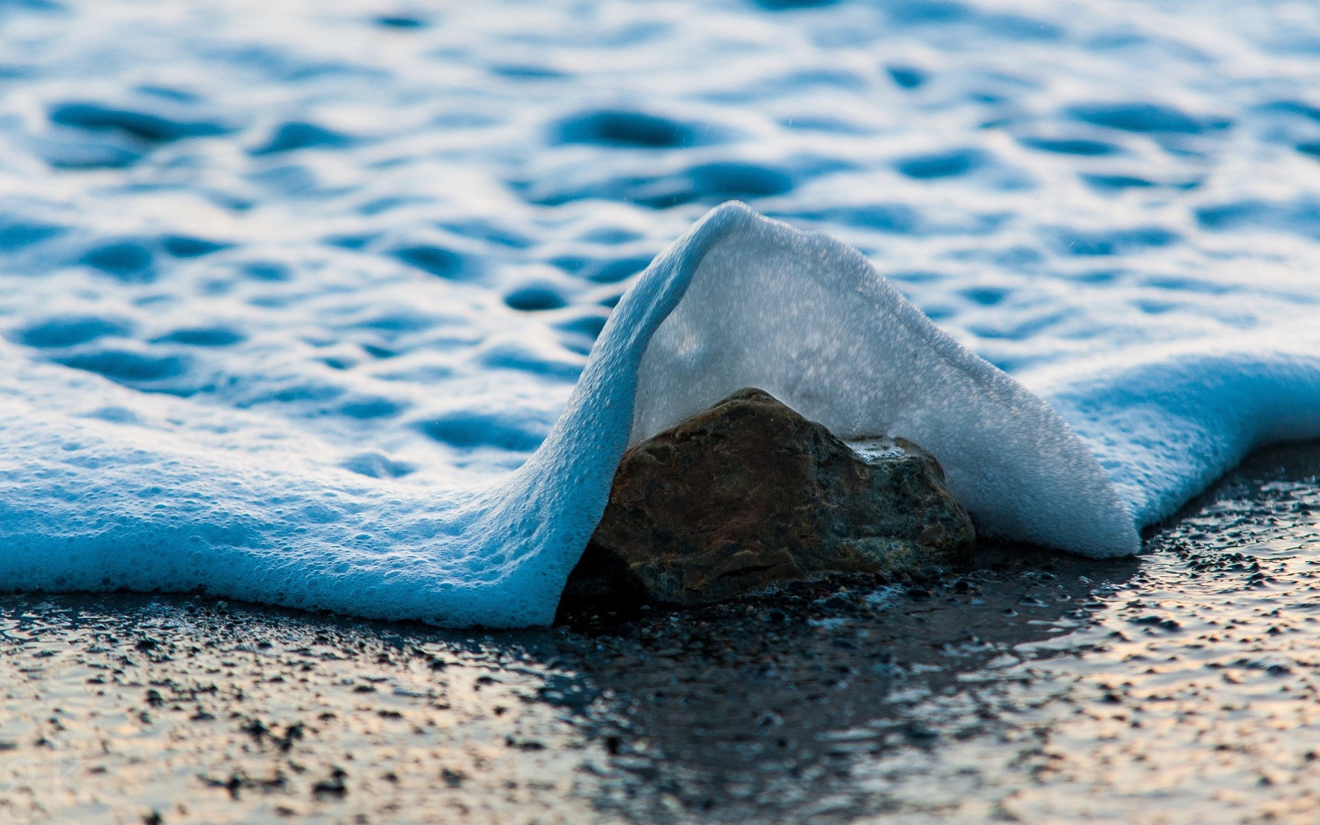 Stone covered by sea foam on a beach HD Wallpaper