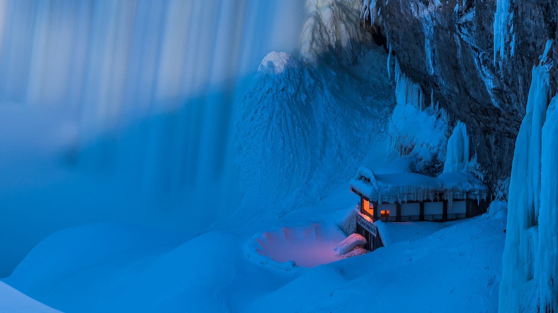 Frozen waterfall with a small illuminated cabin HD Wallpaper