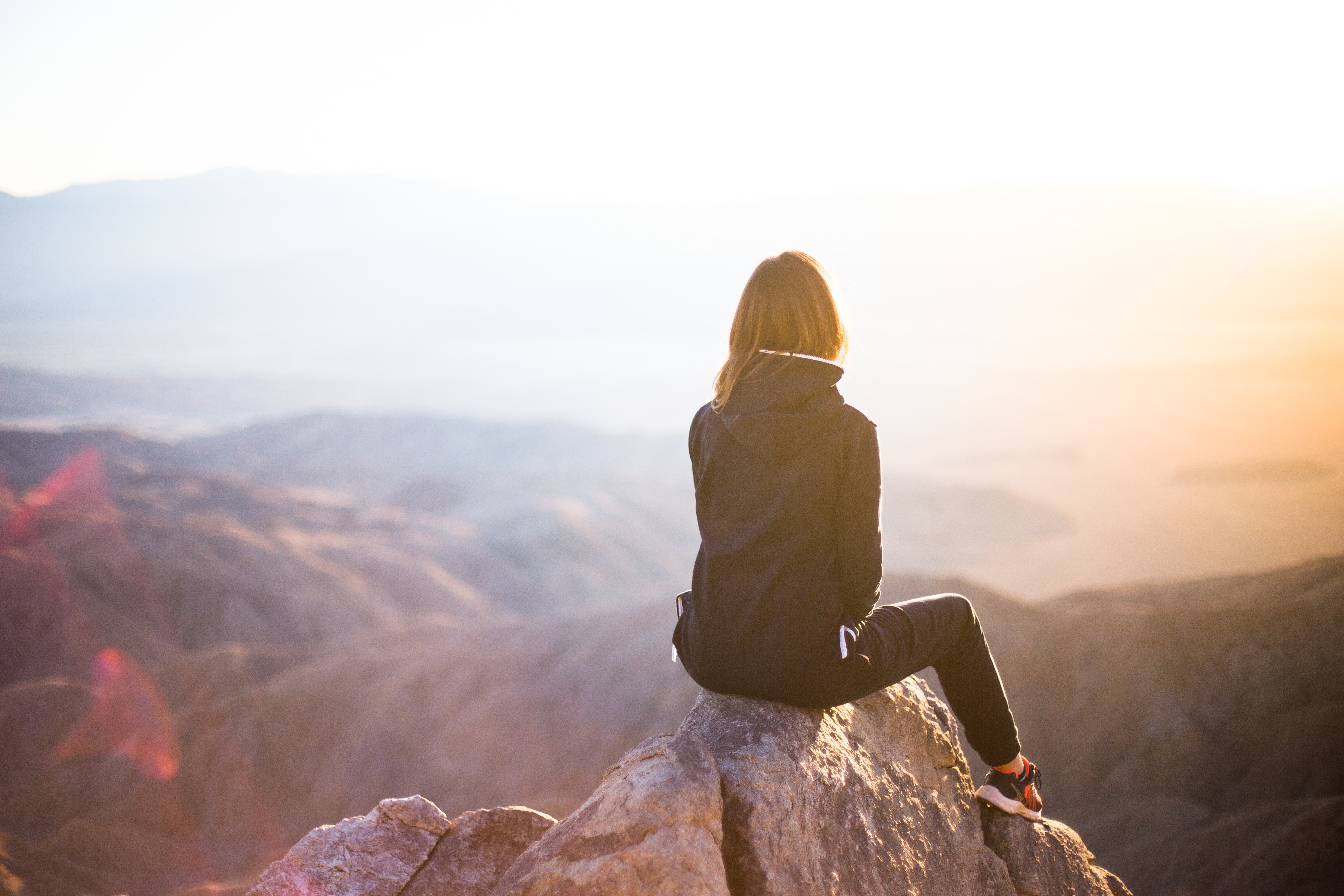 Woman sitting on a rock overlooking mountains at sunrise HD Wallpaper