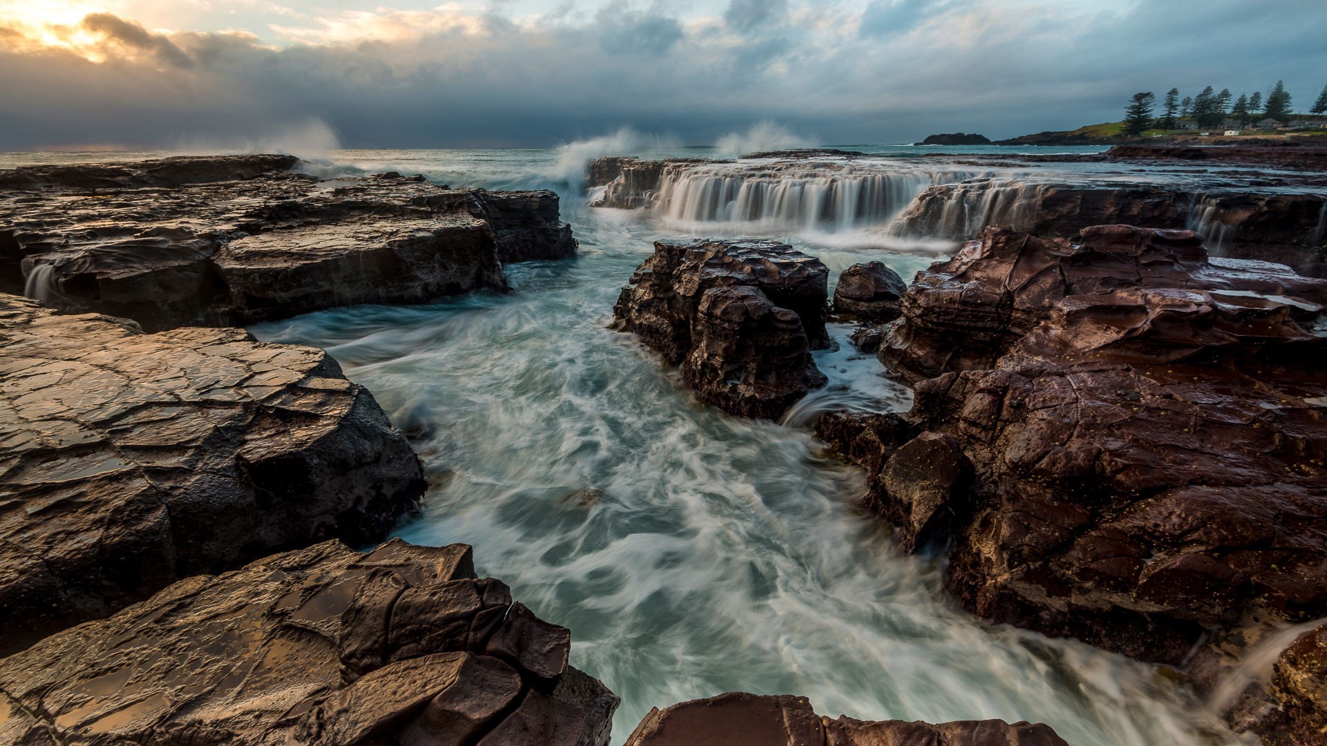Ocean waves crashing over rocky shore with waterfall HD Wallpaper