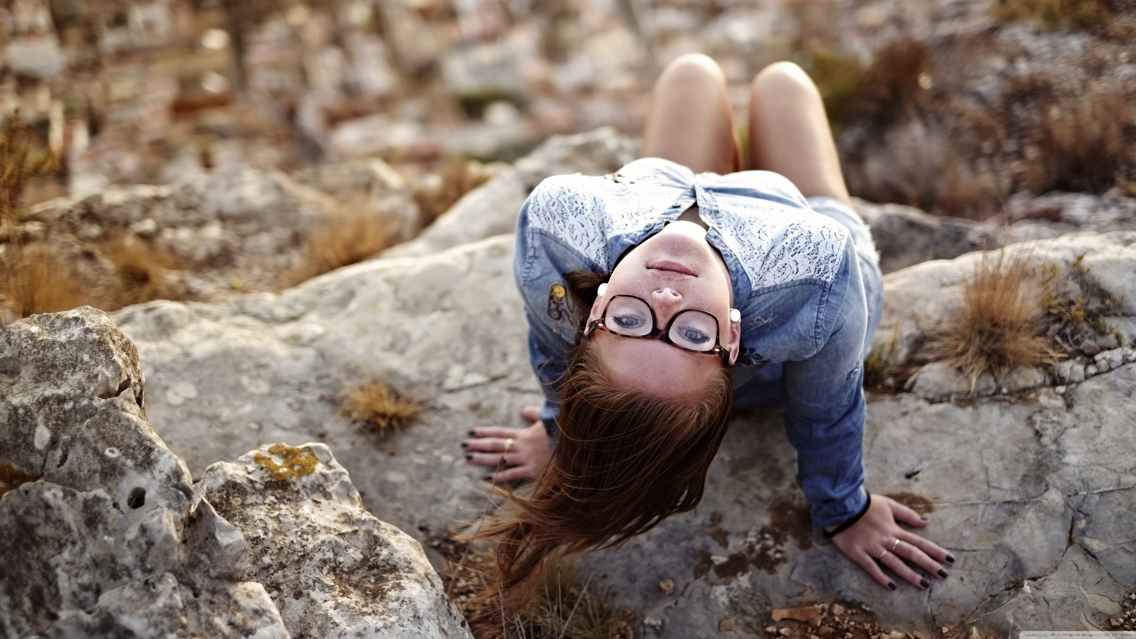 Woman with glasses lying on rocks outdoors HD Wallpaper