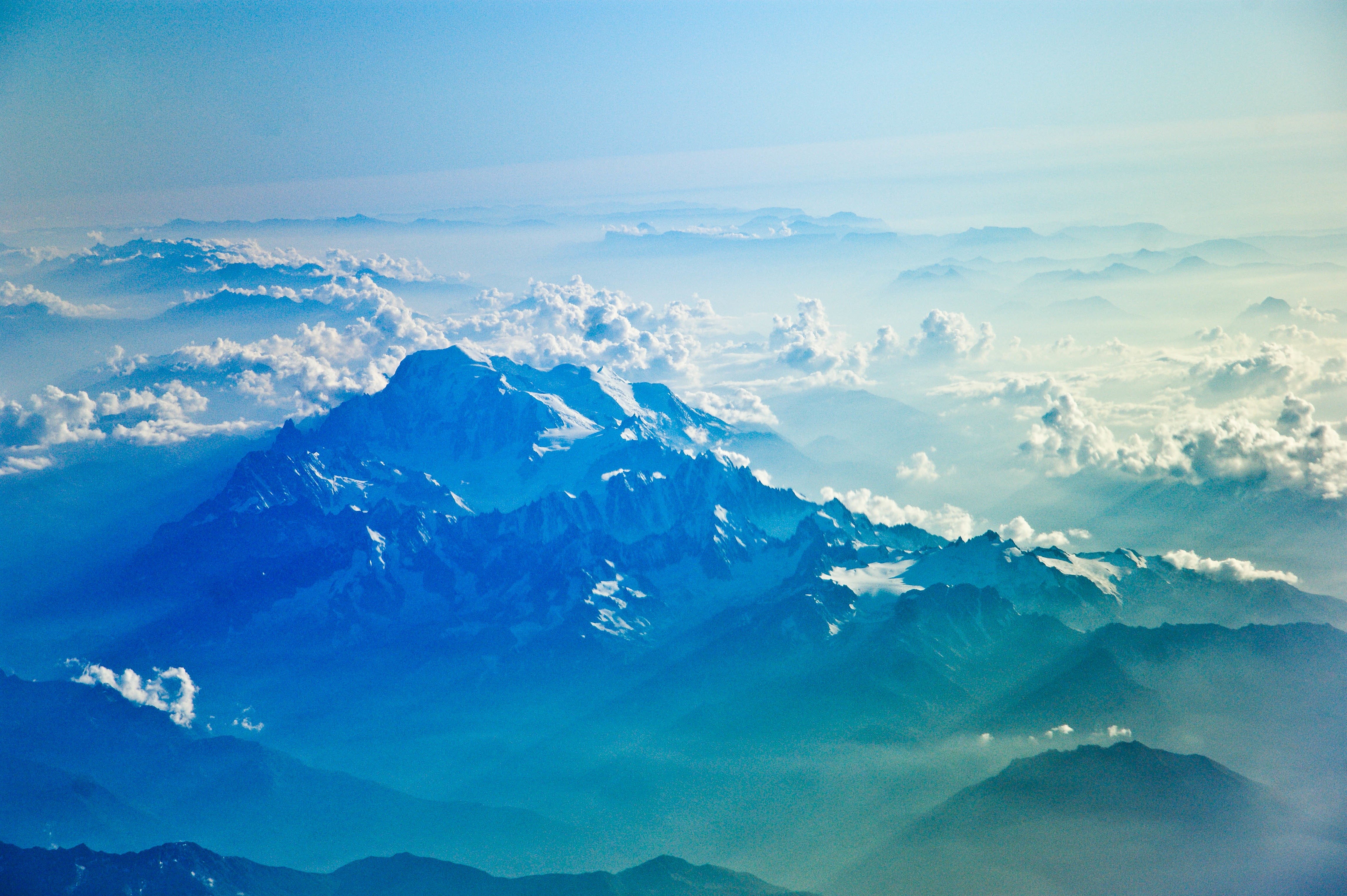 Snow-capped mountains above clouds from an aerial view HD Wallpaper