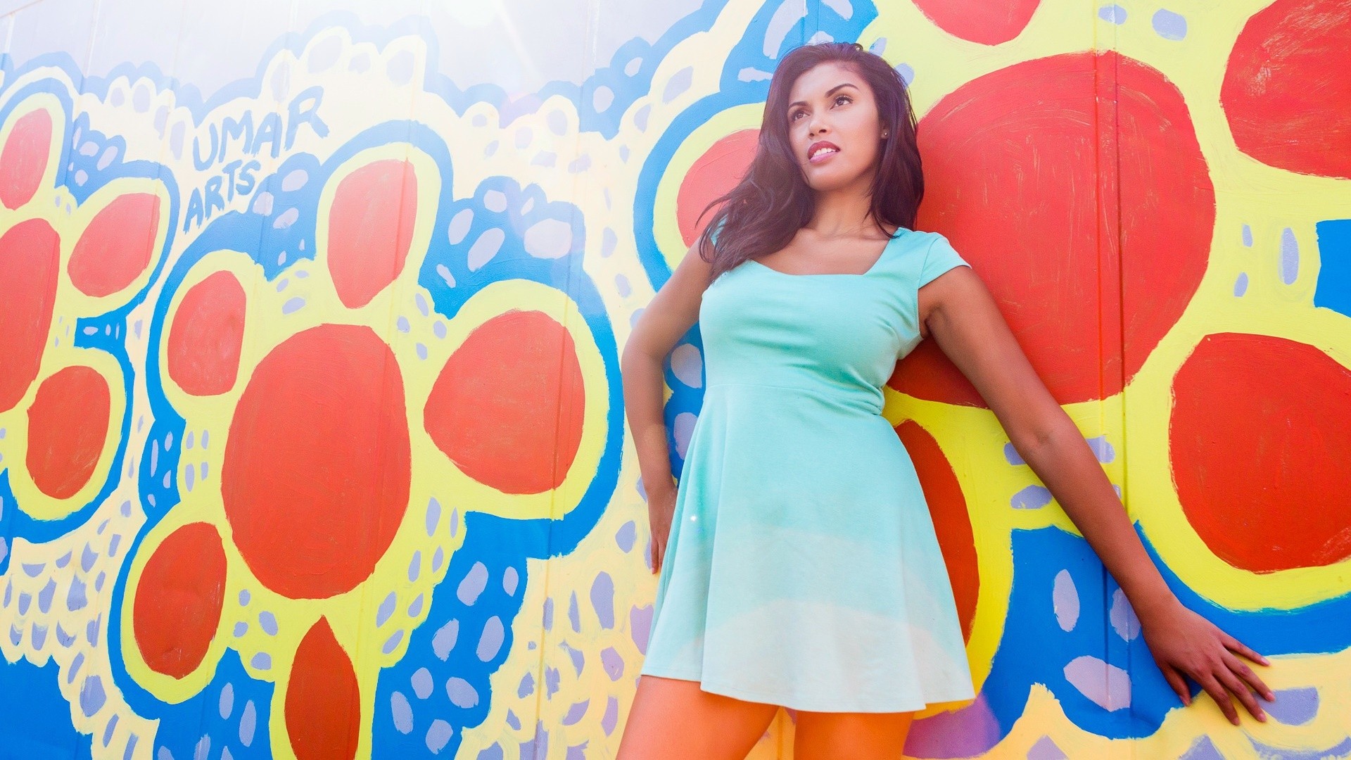 Woman in a mint green dress posing against a colorful mural HD Wallpaper