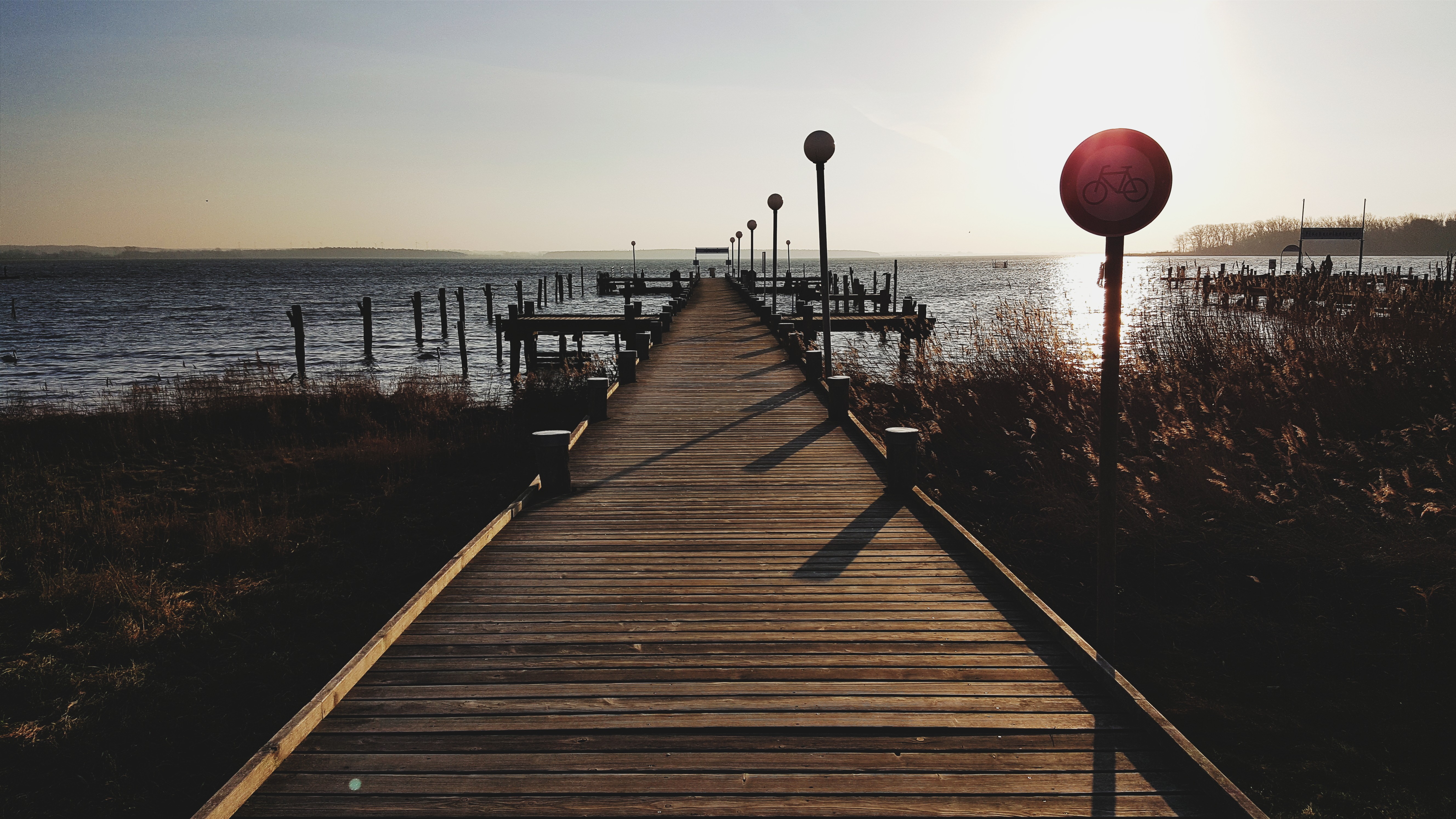 Wooden pier with lampposts and a bicycle sign at sunset HD Wallpaper