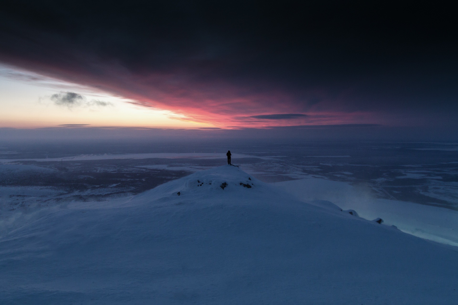 Person standing on a snowy mountain peak at sunset HD Wallpaper