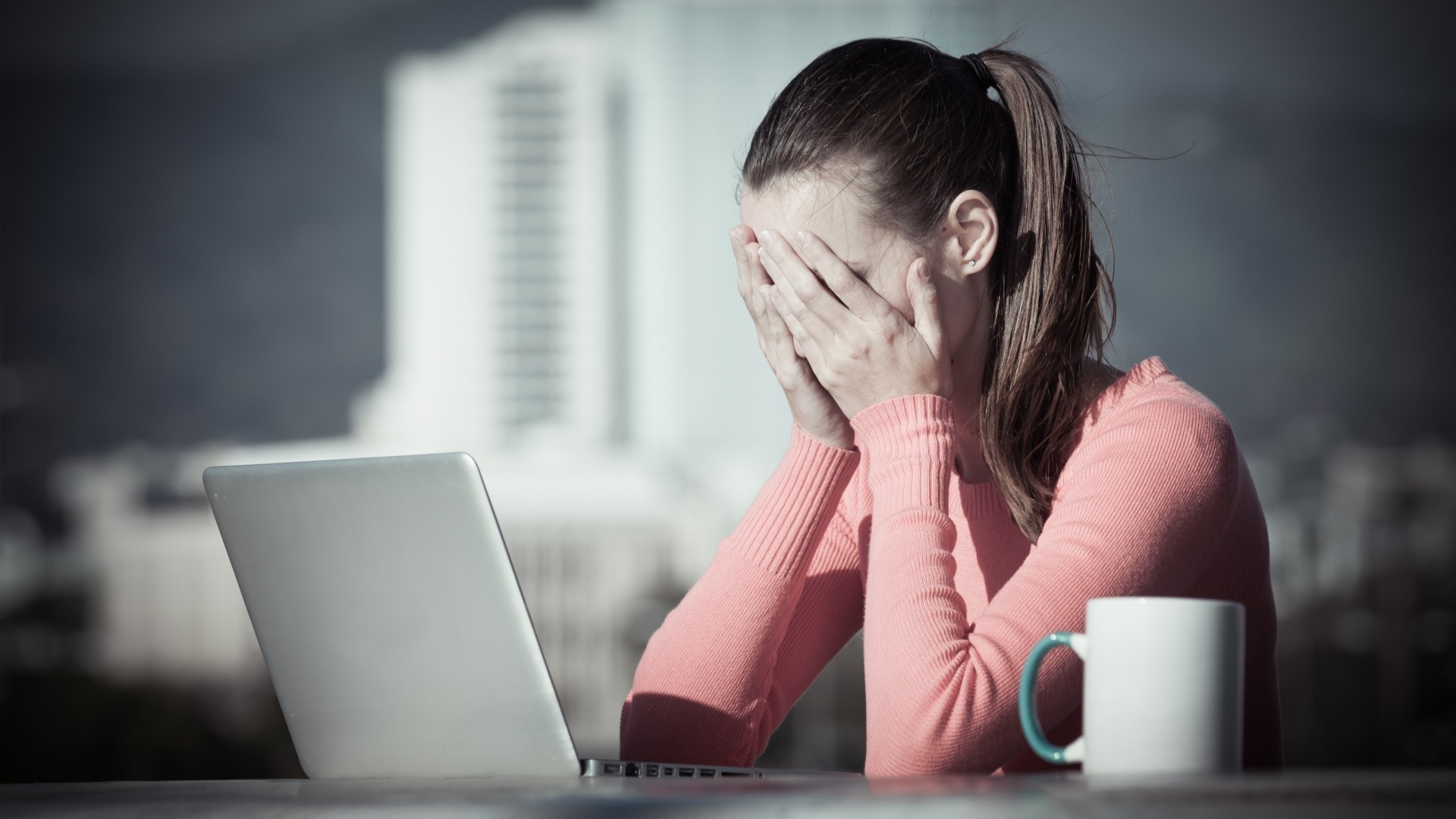 Woman with ponytail covering face with hands at laptop HD Wallpaper