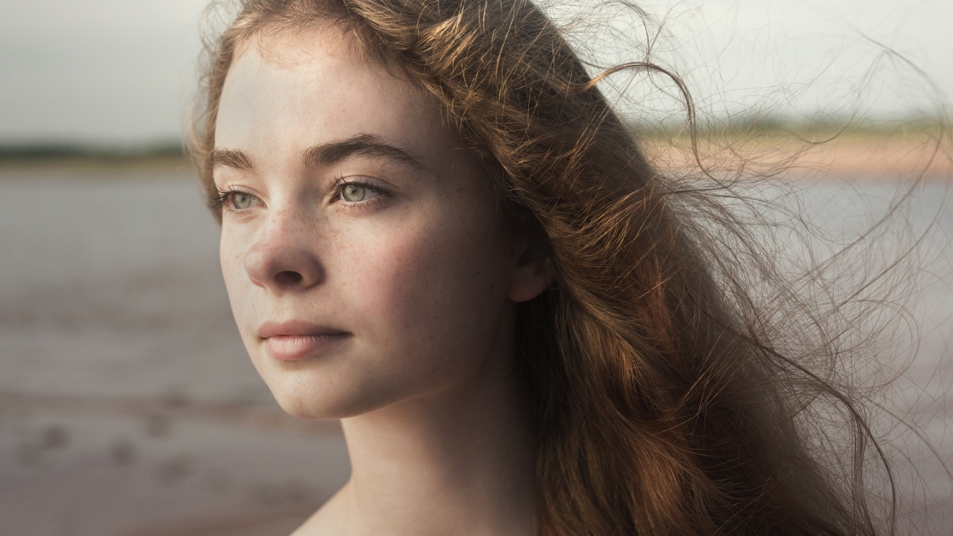 Young woman with freckles and windblown hair outdoors HD Wallpaper