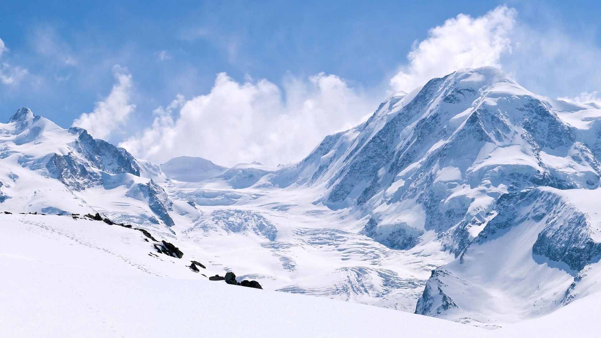 Snow-covered mountains under a blue sky with clouds HD Wallpaper