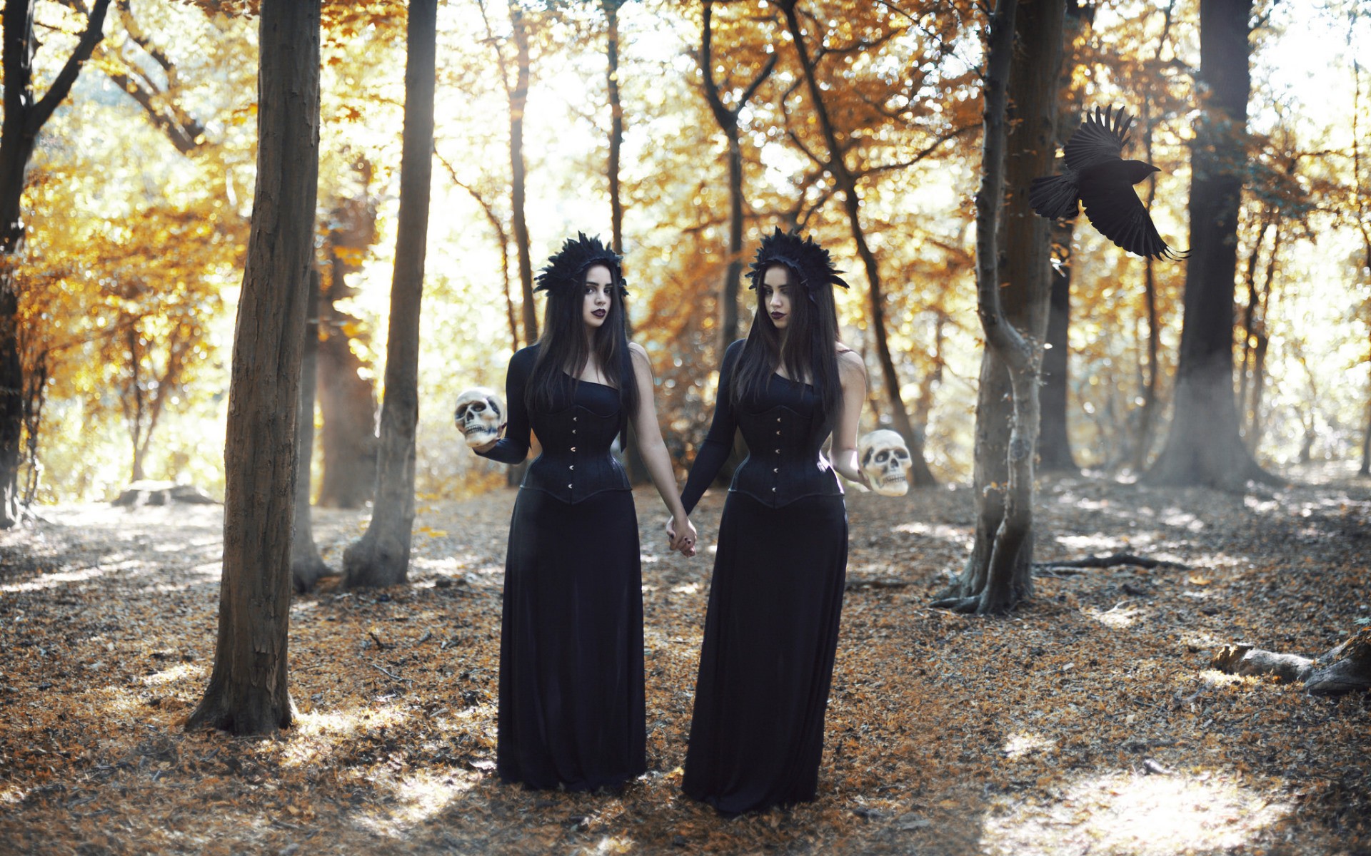 Two women in black dresses holding skulls in a forest with a crow HD Wallpaper