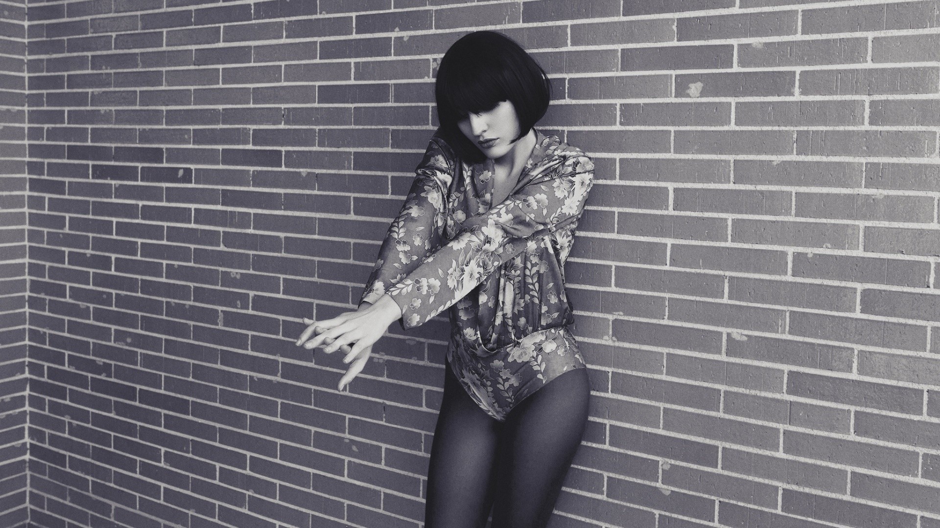 Woman in floral leotard leaning against brick wall HD Wallpaper