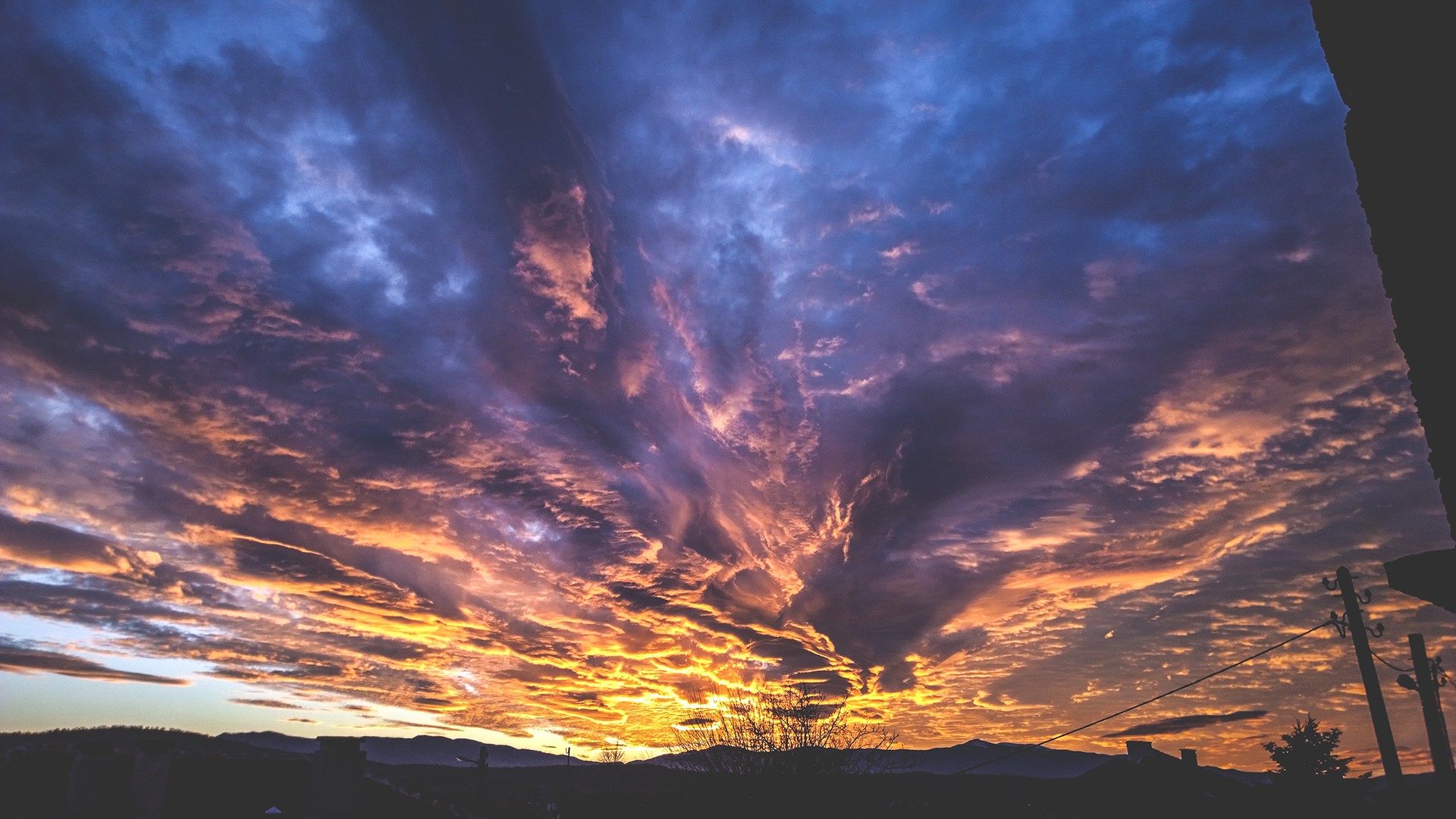 Dramatic sunset sky with clouds over a silhouetted landscape HD Wallpaper