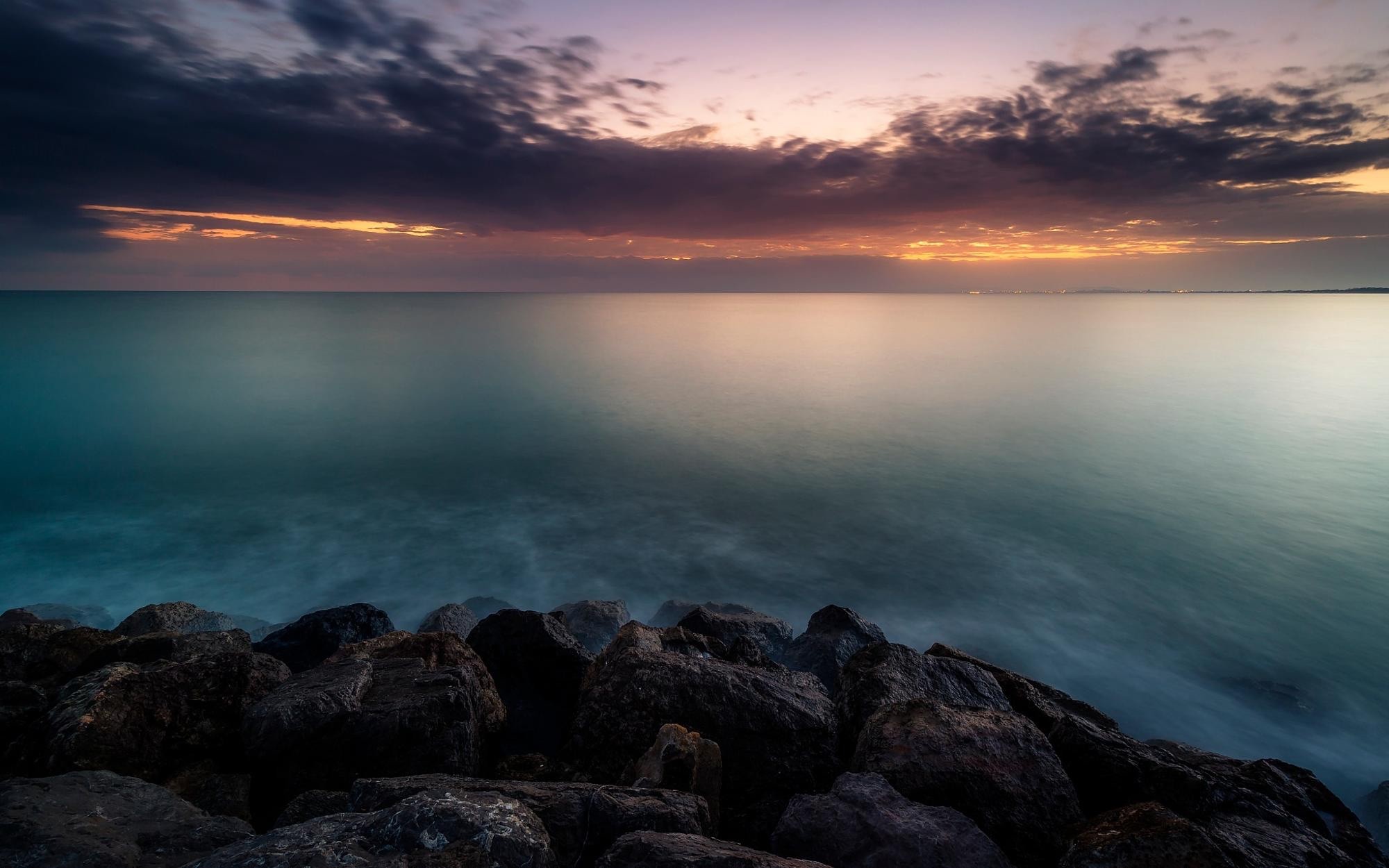 Rocky shore at sunset with calm ocean and clouds HD Wallpaper