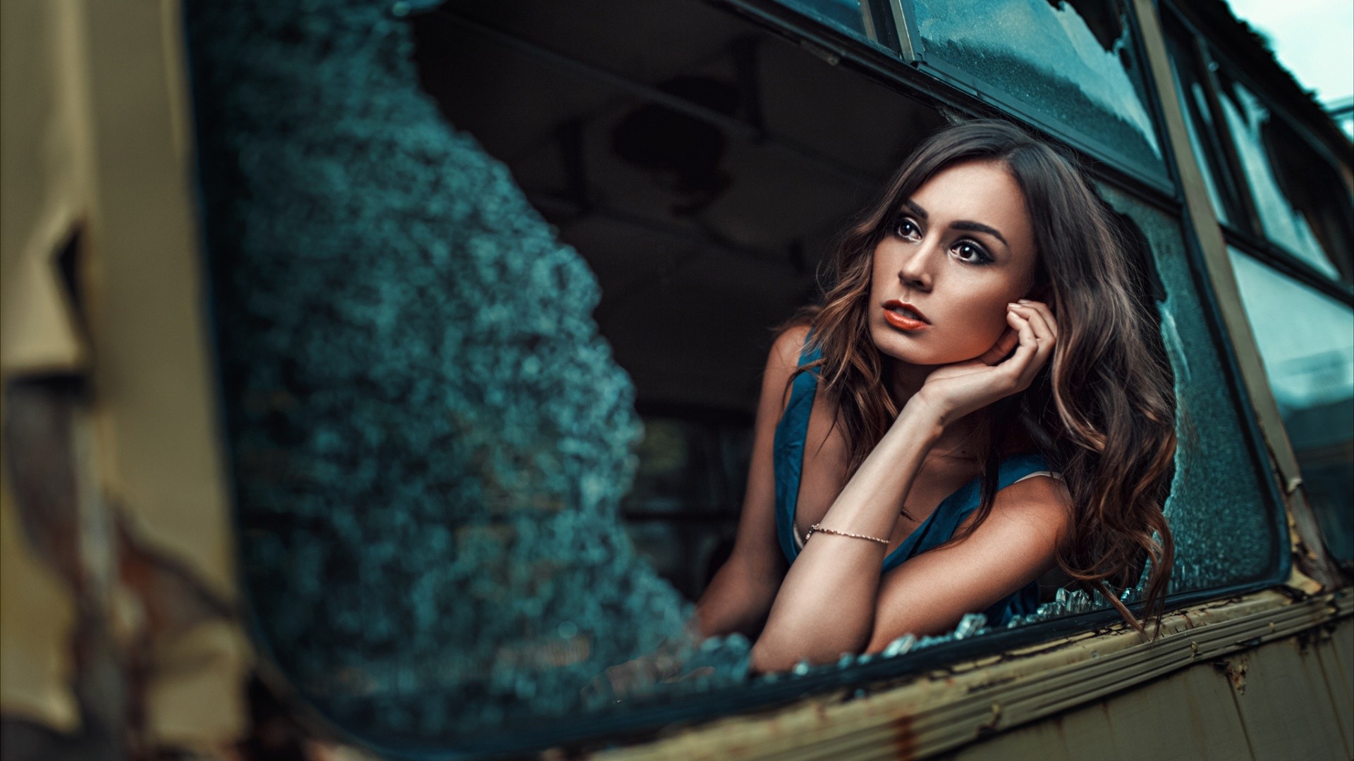 Woman with wavy hair in a blue dress looking out a broken window HD Wallpaper