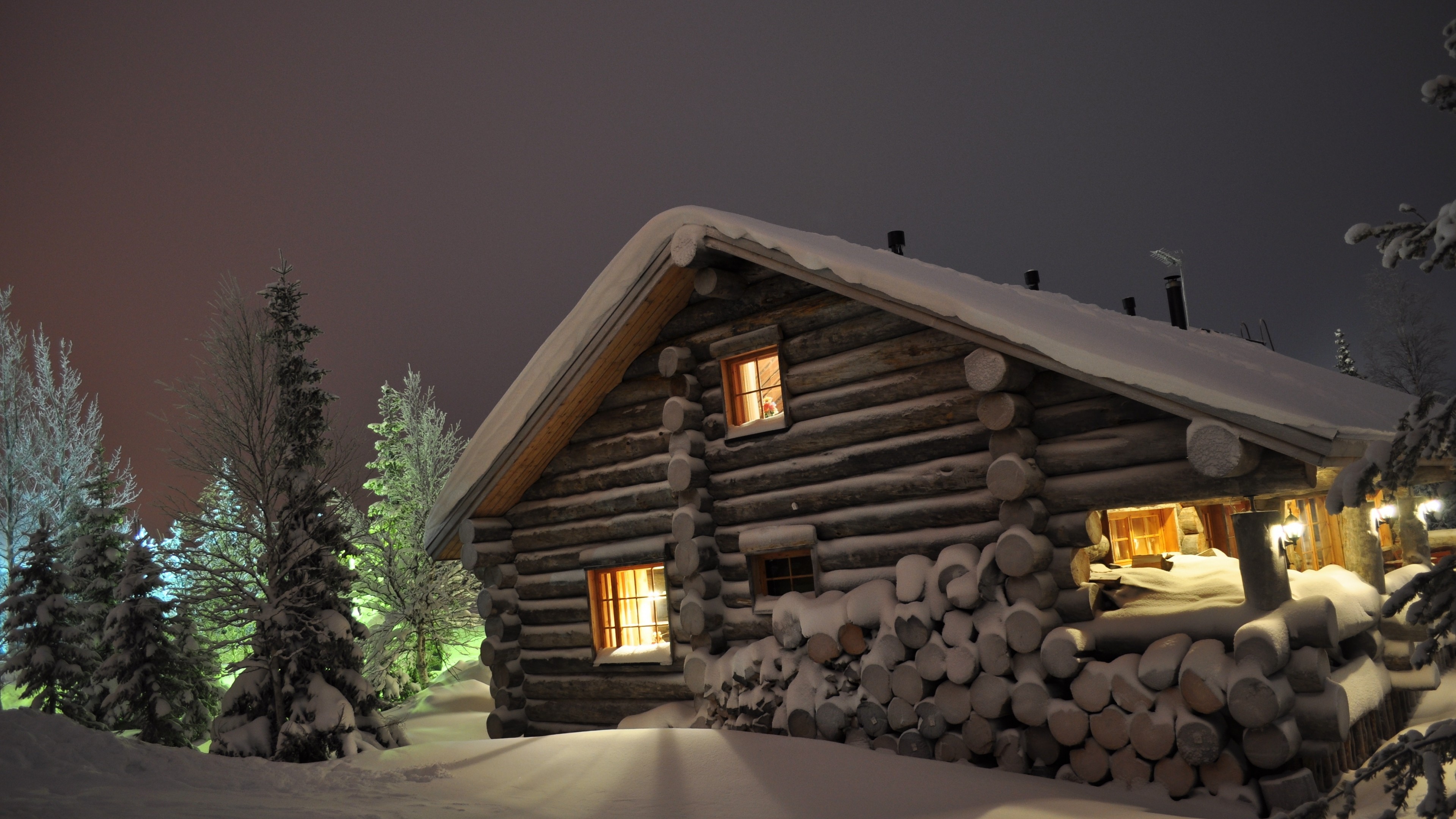Snowy log cabin at night with warm lights HD Wallpaper