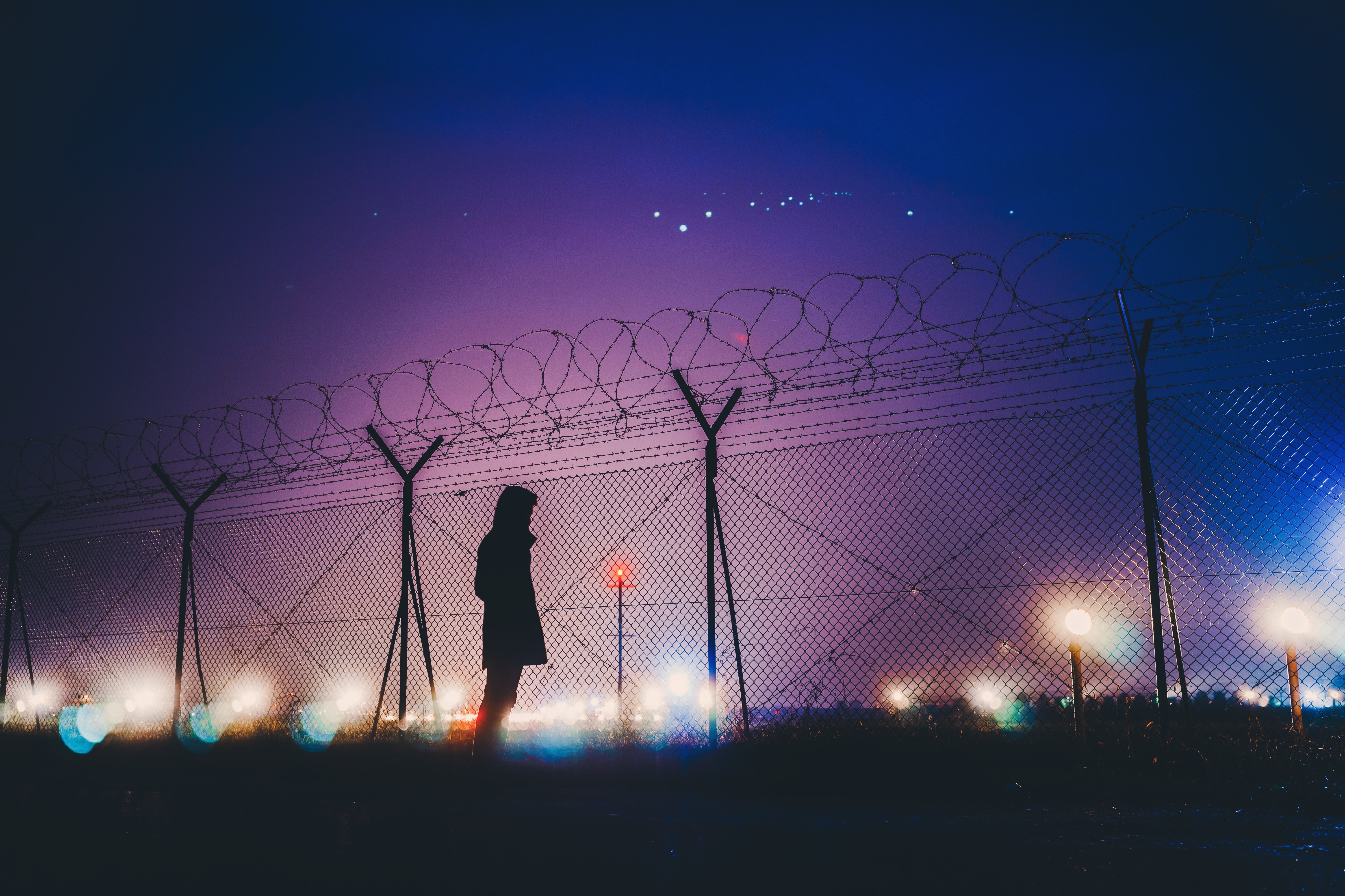 Silhouette of a person by a barbed wire fence at night HD Wallpaper