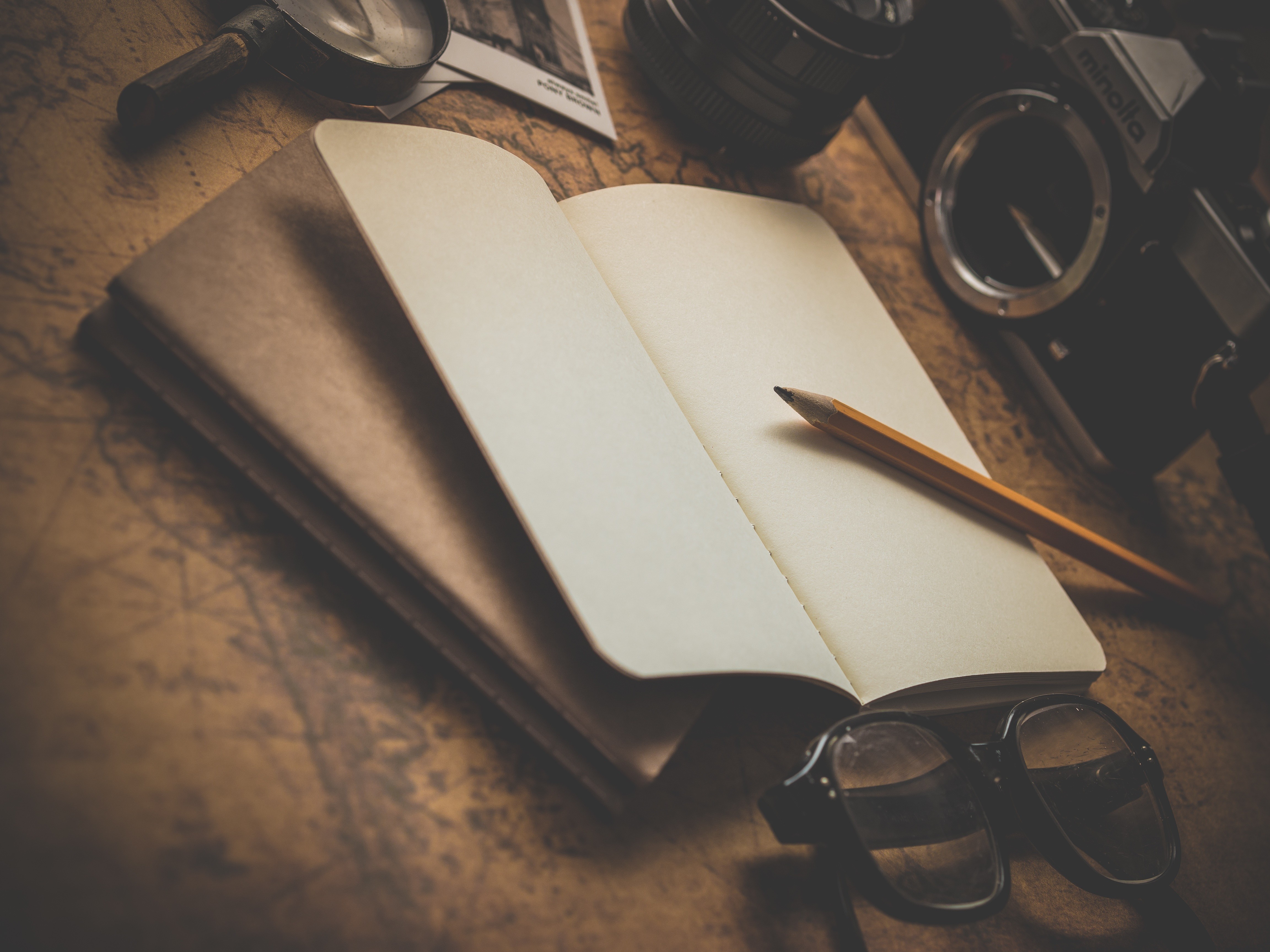 Open notebook with pencil, camera, and glasses on map HD Wallpaper
