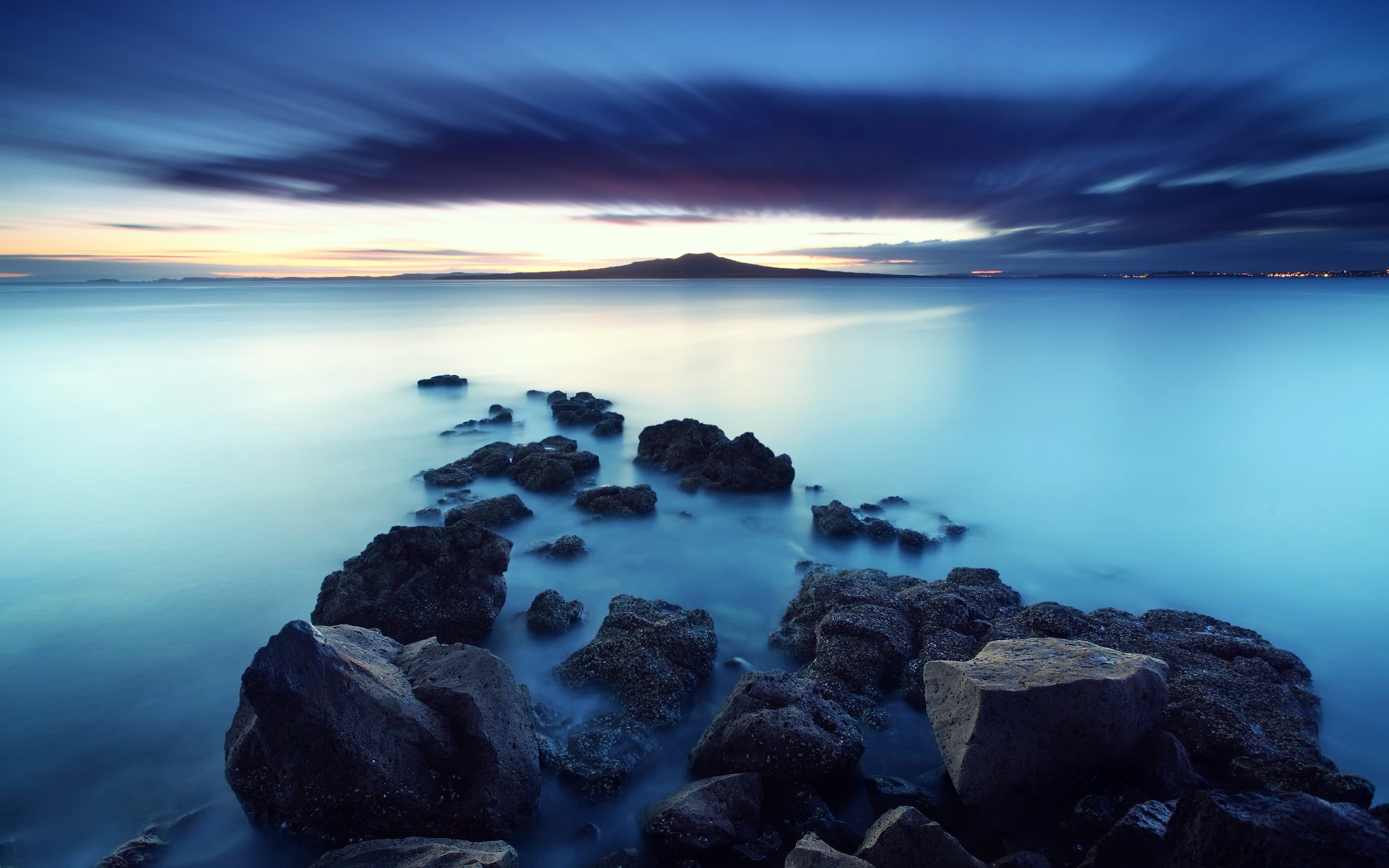 Rocky coastline at dusk with distant mountain HD Wallpaper