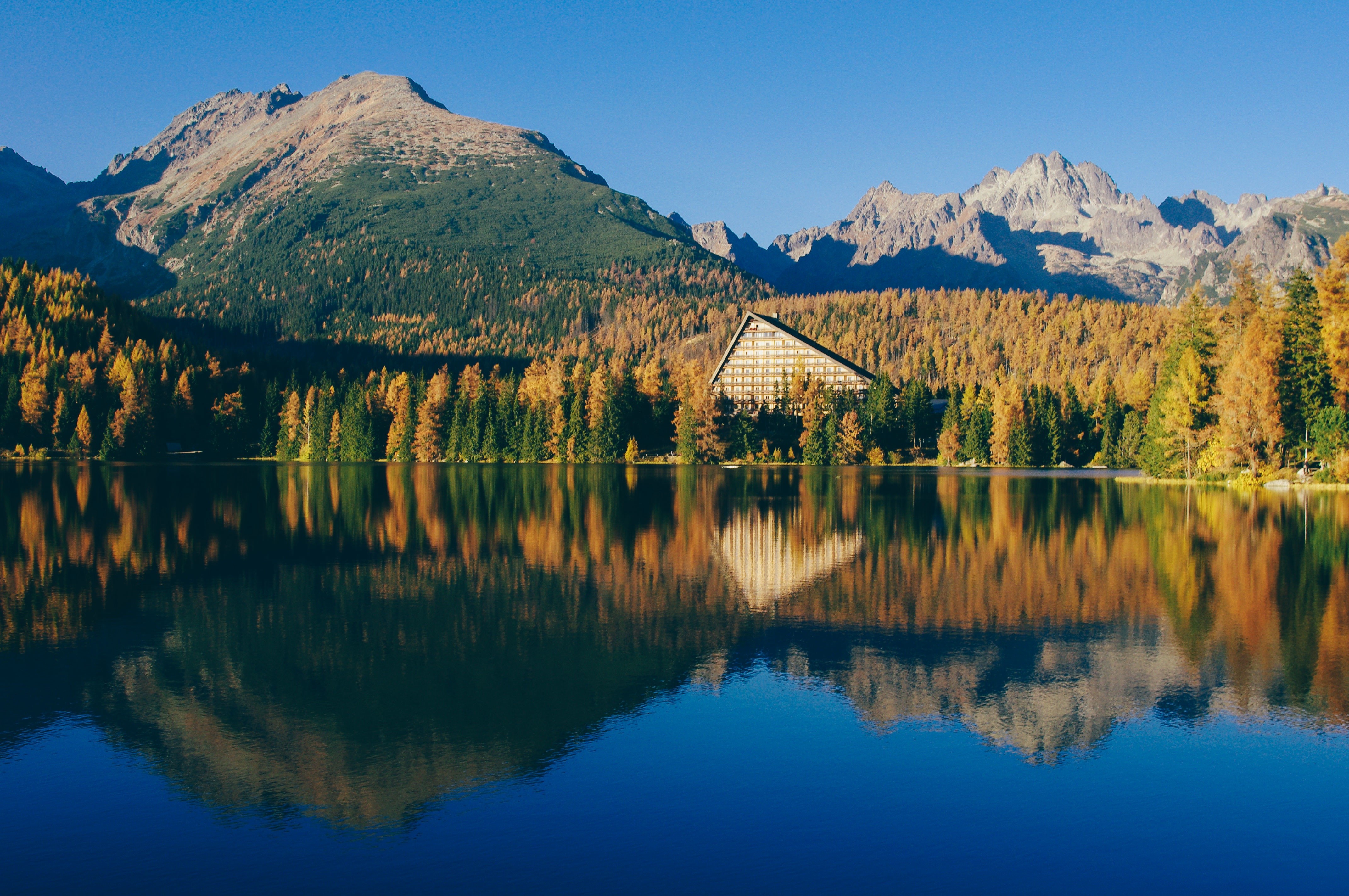 Lake and mountains with autumn trees and a hotel HD Wallpaper