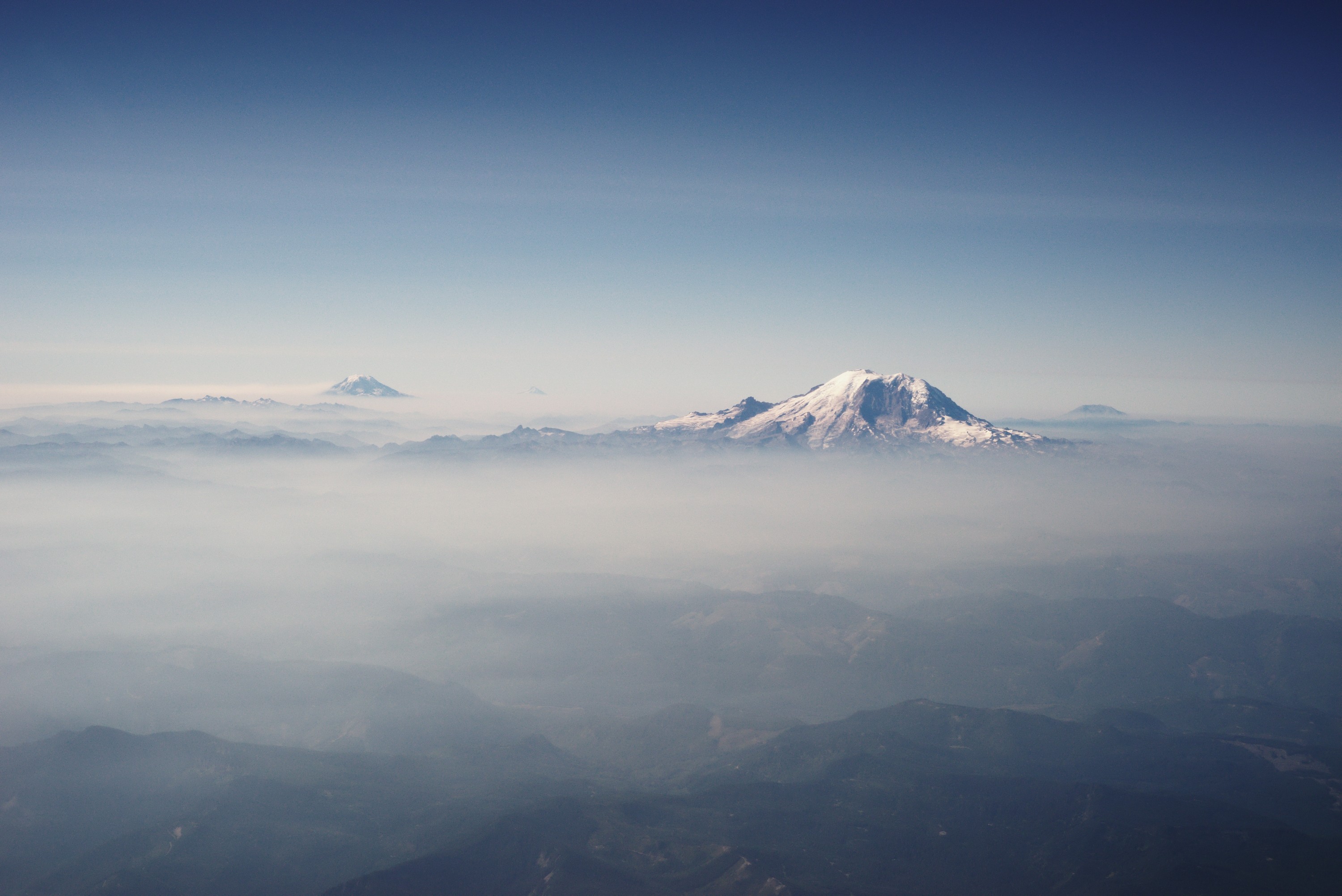 Snow-capped mountains emerge from mist under a clear blue sky. HD Wallpaper