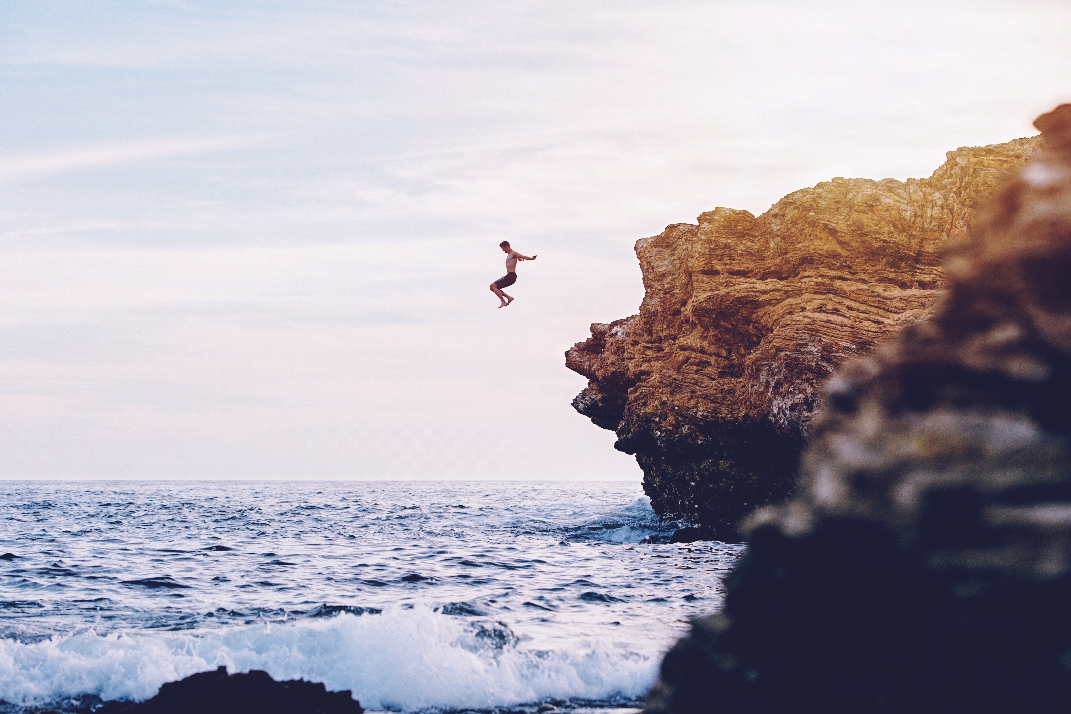 Man jumping off a cliff into the sea HD Wallpaper