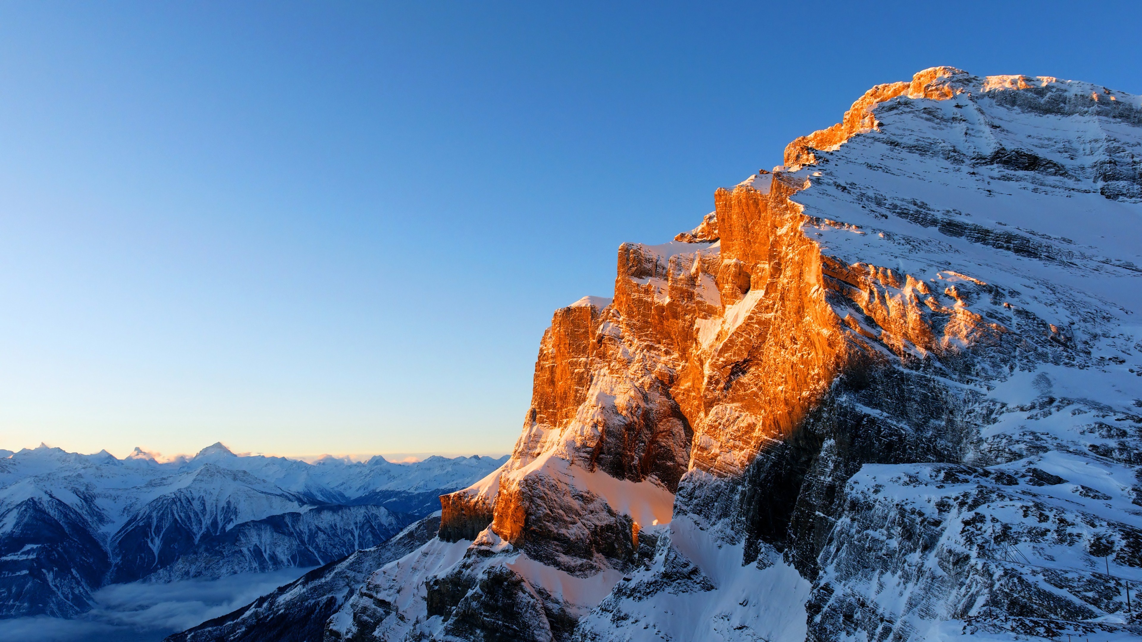 Snowy mountain peak illuminated by golden sunlight HD Wallpaper